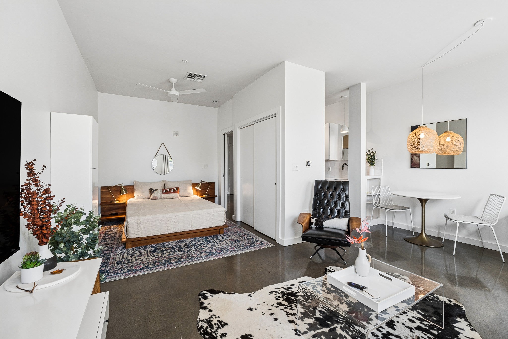 Studio layout with a platform bed, built-in closet, dining table and desk area under a window with light-filtering shades
