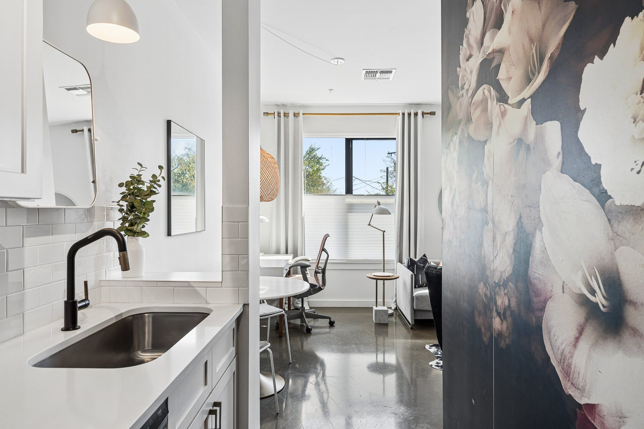 Kitchen with white countertops, a stainless steel sink with a black faucet and a floral wall mural beside the galley