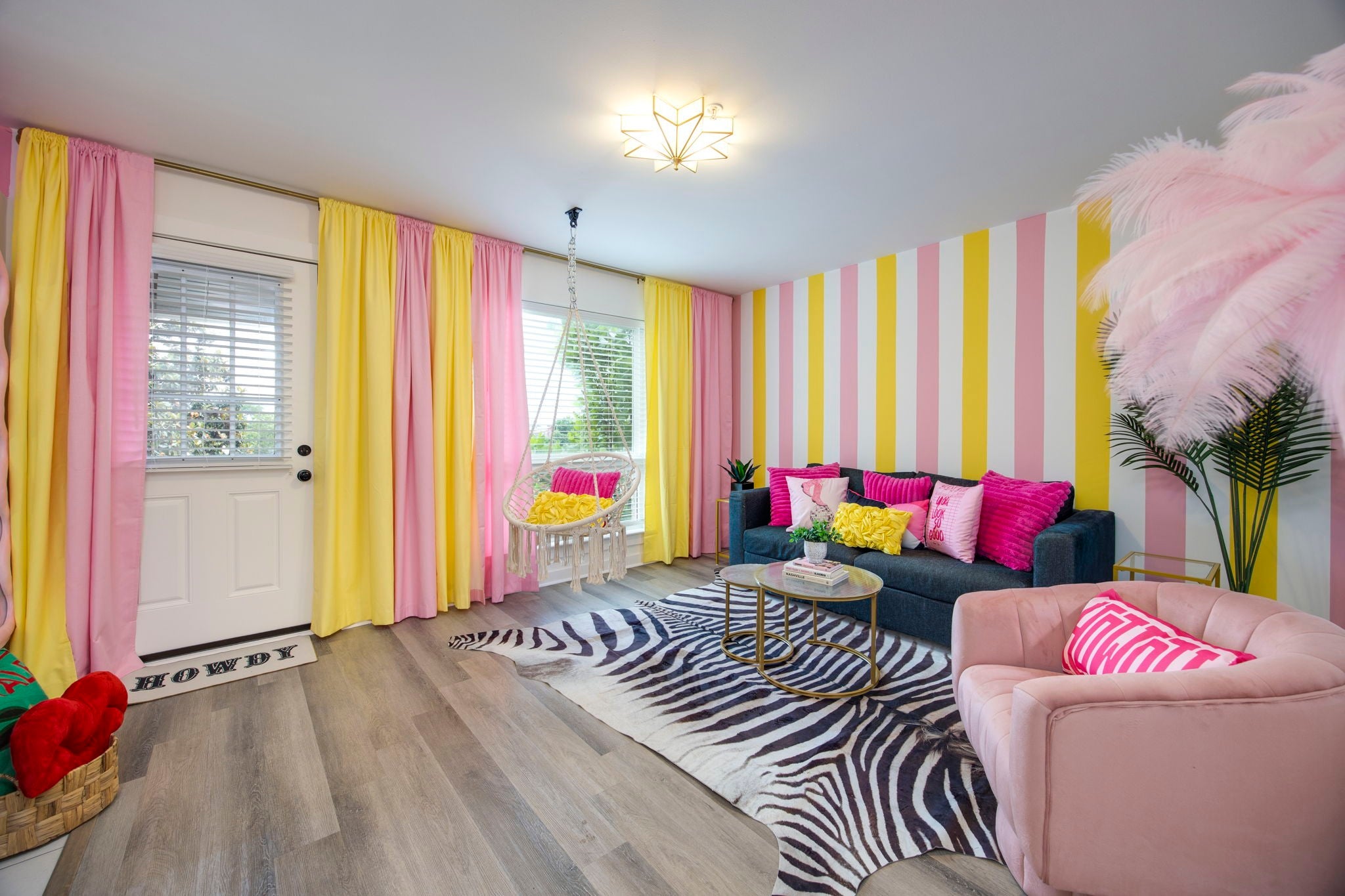 Living room with pink and yellow curtains, a hanging chair by the window, a dark sofa and a zebra-print rug on wood floors