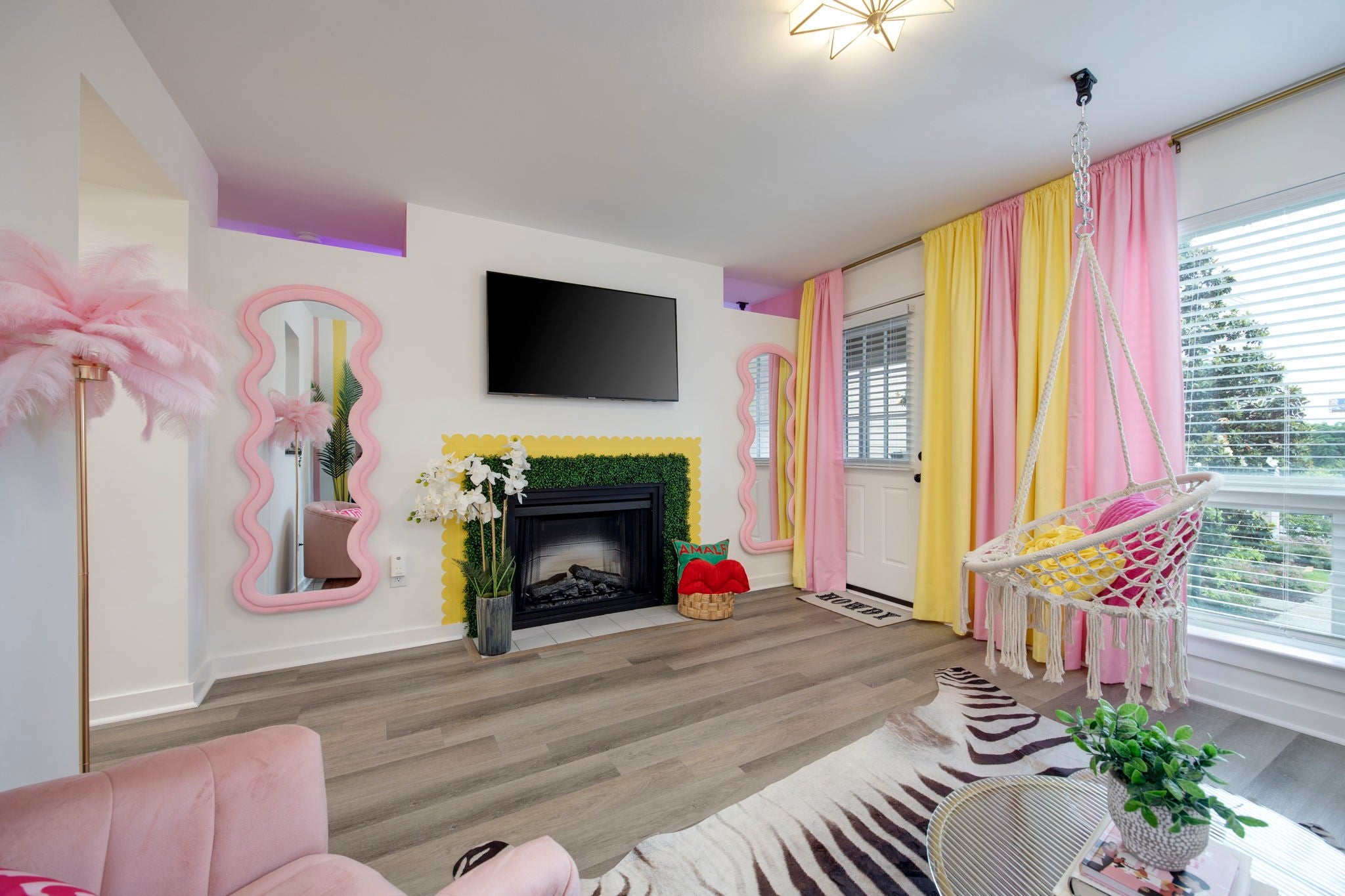 Living room with a built-in fireplace, a wall-mounted television, a hanging rope chair and wavy pink mirrors