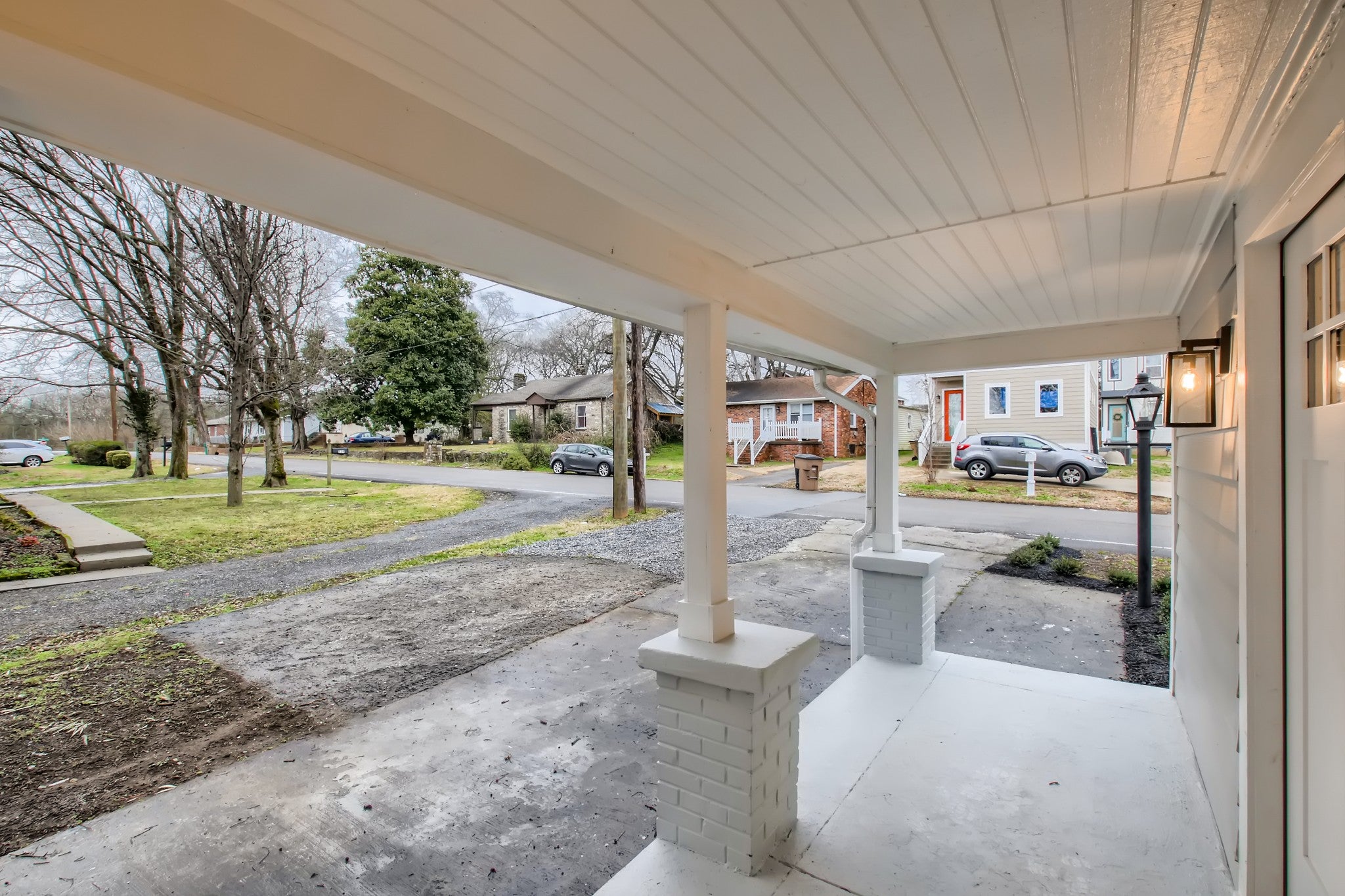 Covered porch looking out over a gravel drive and a grassy front yard toward neighboring homes on the street