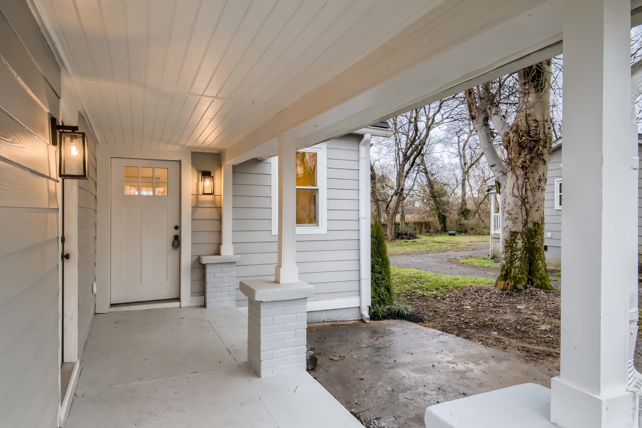 Covered front porch with a white beadboard ceiling, a six-pane front door and brick porch columns