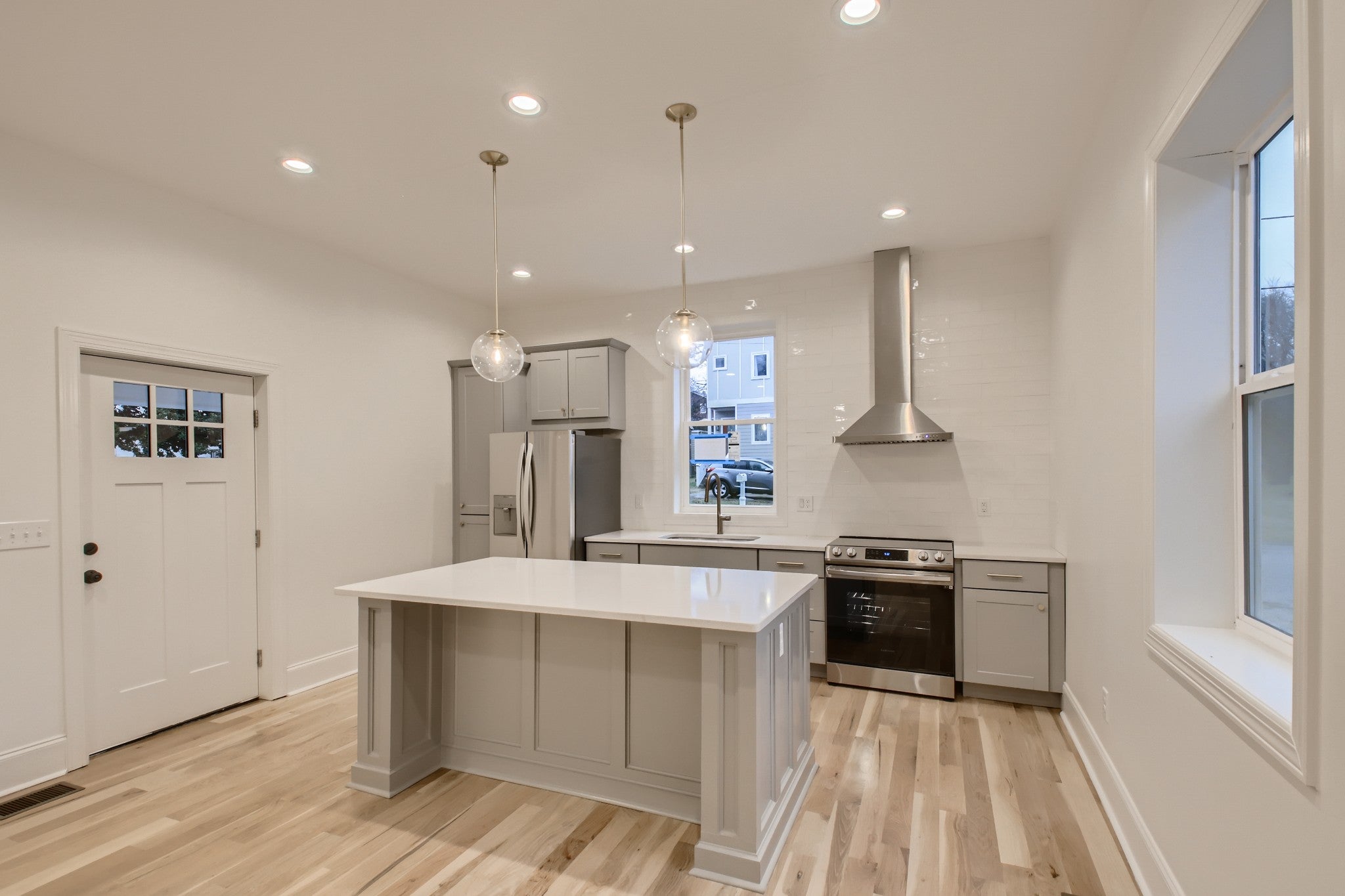Kitchen with a center island, gray cabinets, white stone countertops and stainless steel range and hood