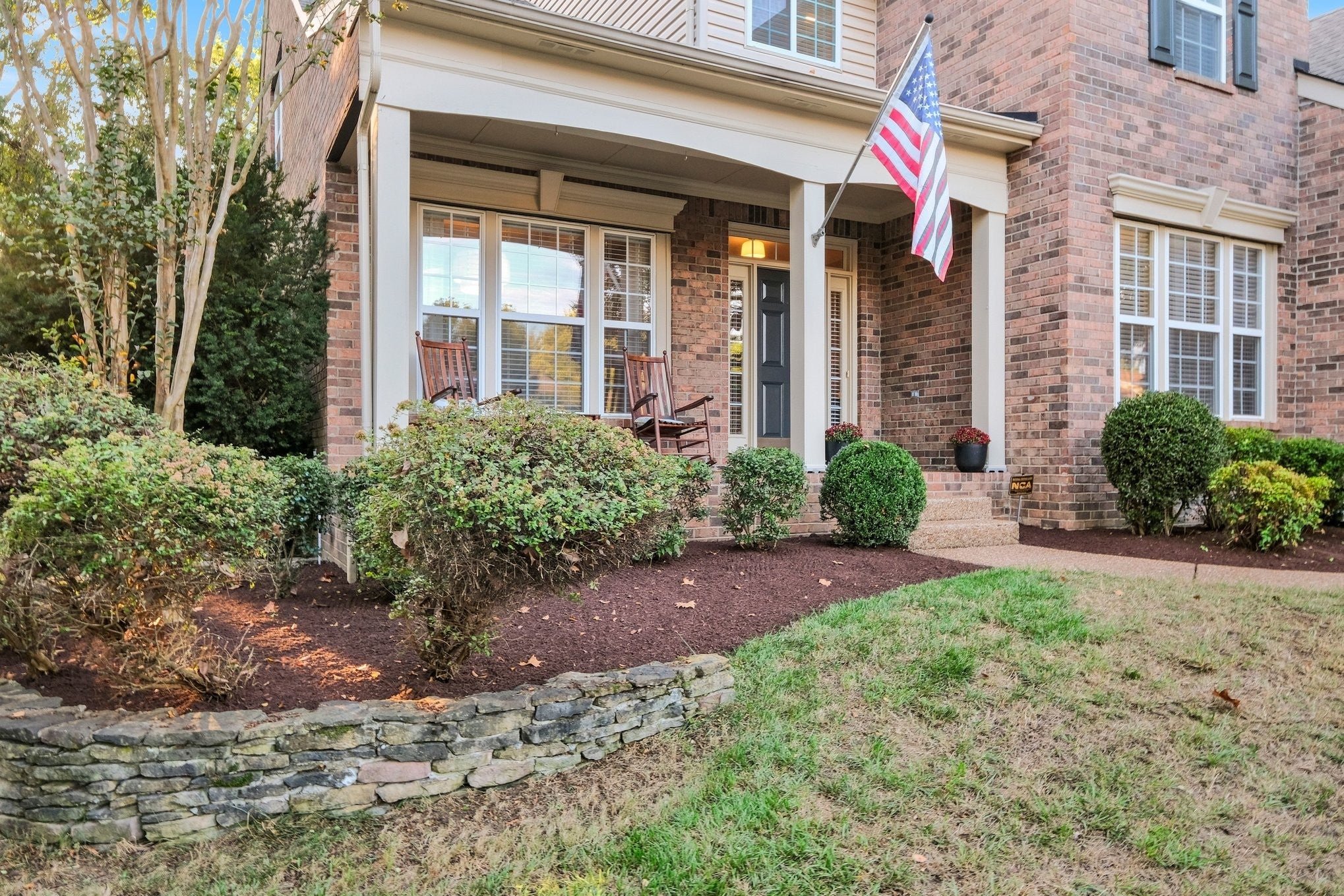 5-bed home for sale in Franklin, TN 37064, 403 William Wallace Dr Covered front porch with brick walls, a wooden rocking chair, shrubs and a stone retaining wall along the walkway