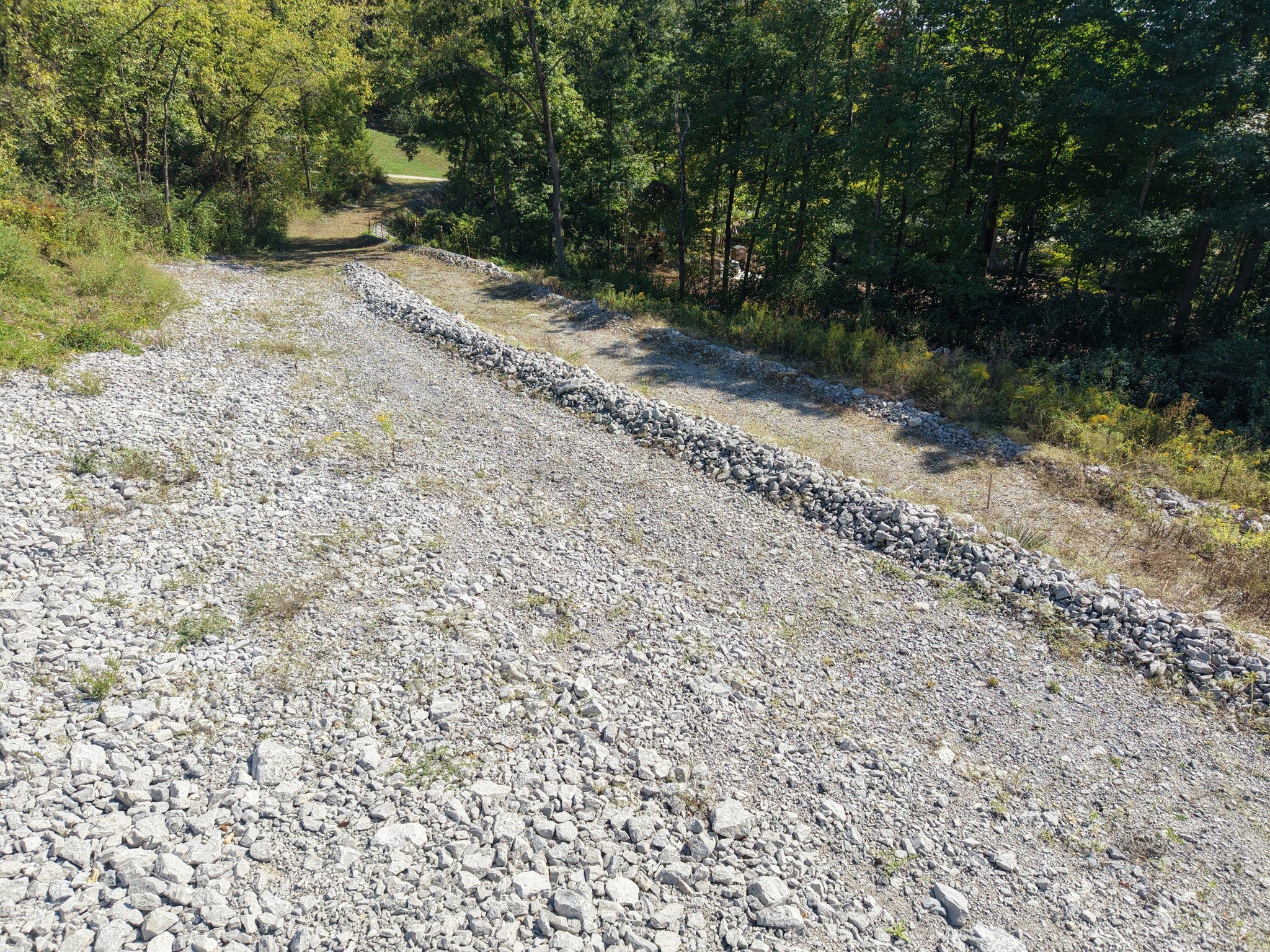 lot for sale in Brentwood, TN 37027, 1765 Woodsong Dr Gravel roadway edged by a long row of stacked stone along a sloped, partly grassy embankment