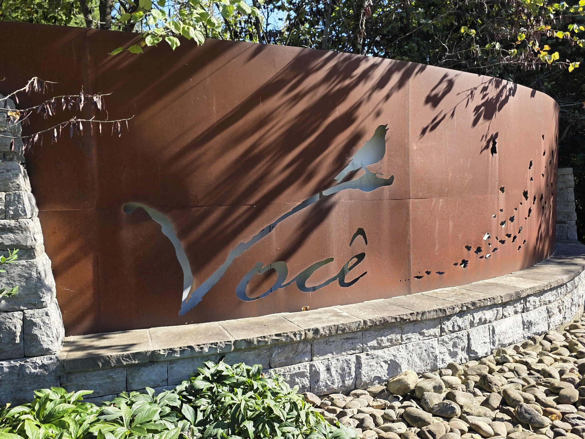 lot for sale in Brentwood, TN 37027, 1765 Woodsong Dr Dark rust-colored metal wall with a cut-out bird on a branch and the word Voce, set against stacked stone and river rock