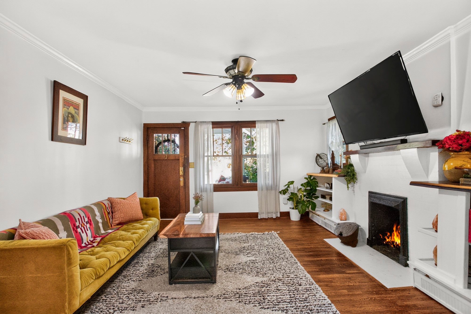 Living room with a white fireplace, wood floors and a front door with a glass panel and a window with sheer curtains