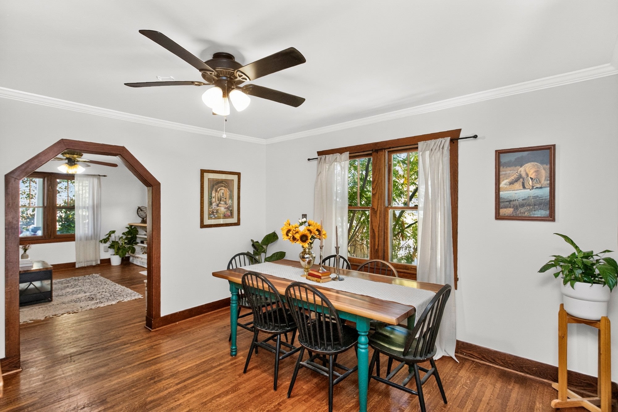 Dining room with wood floors, crown molding, a green table and six chairs beside an arched doorway to the living room