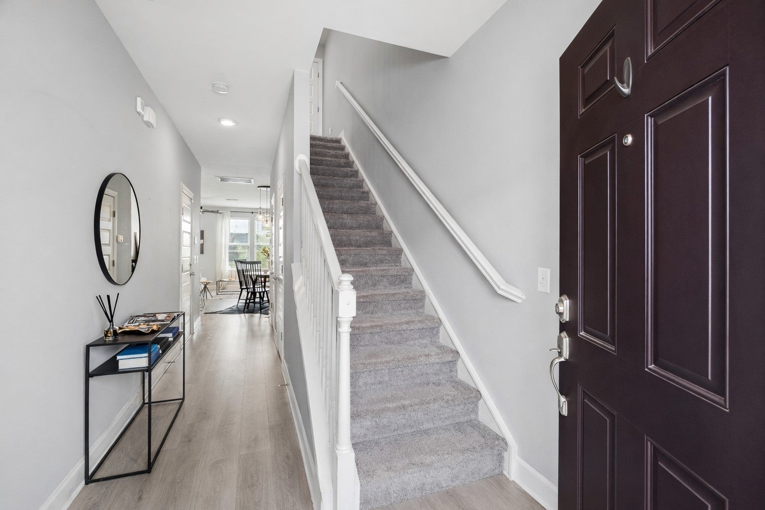 Entry hall with wood-look flooring, a staircase with carpeted treads and white rails, and a round wall mirror