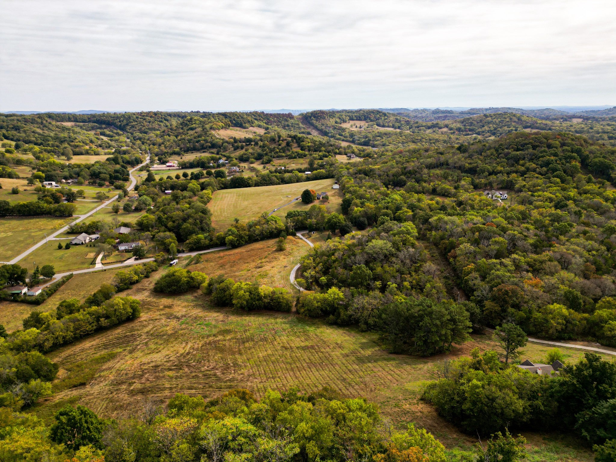 Aerial view of rolling wooded hills with cleared fields and scattered houses in the distance