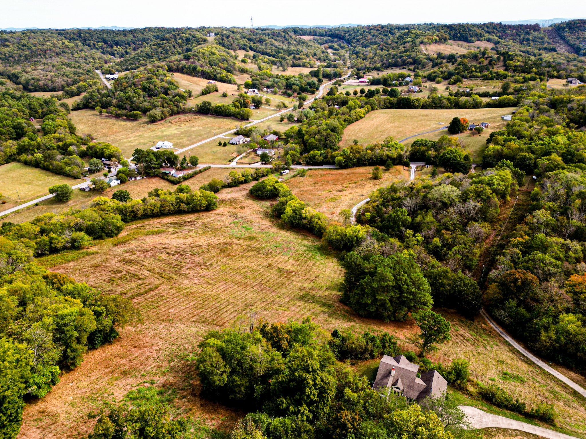 Aerial view of cleared field beside tree line with a single house at the lower right corner