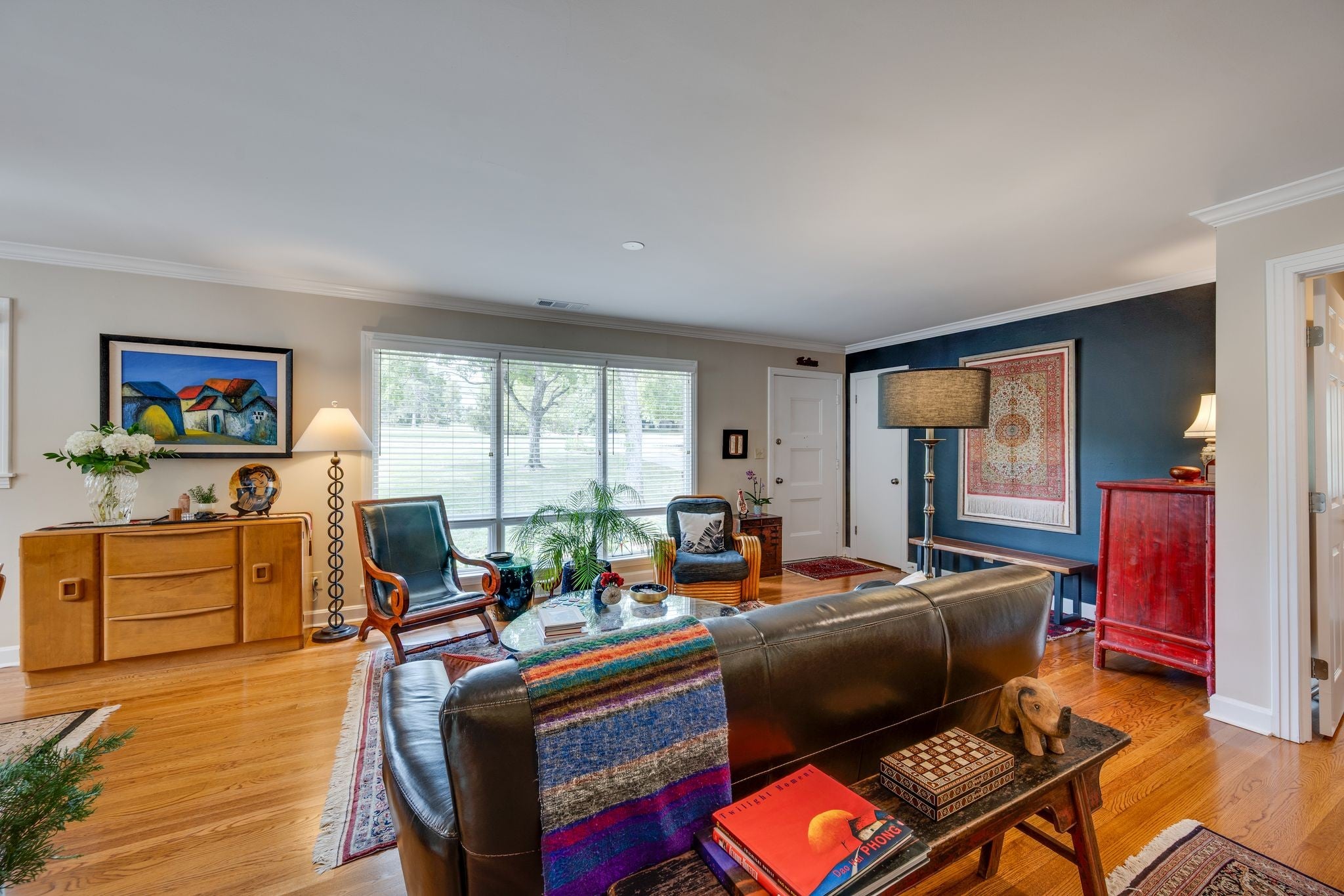 Living room with wood floors, a dark accent wall, a sideboard and a wide window with blinds