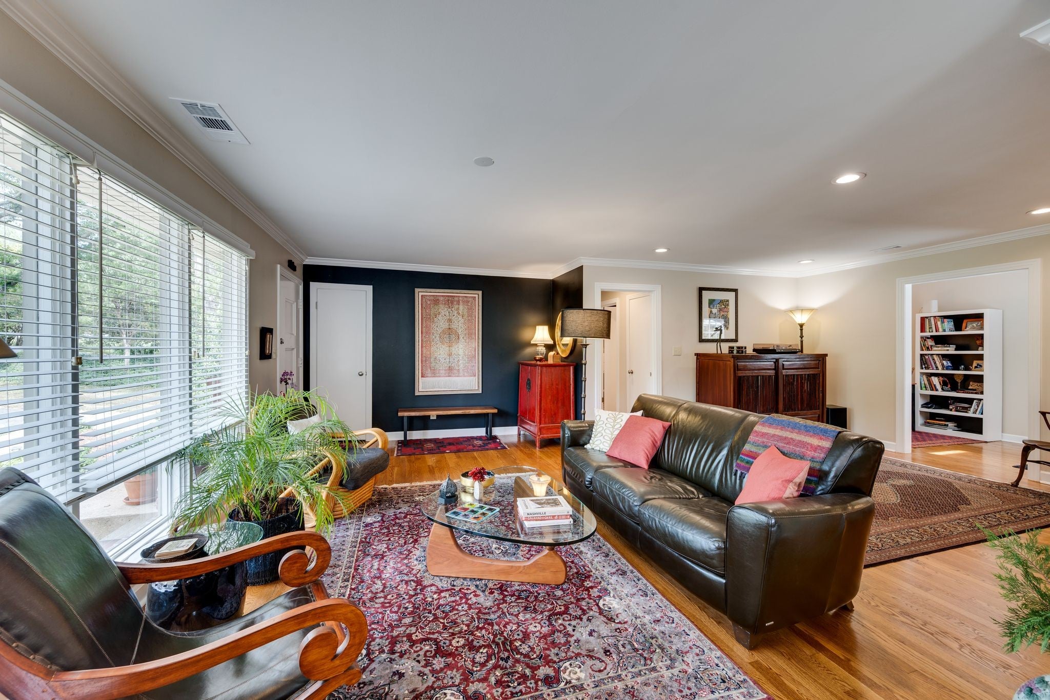 Living room with wood floors, a large window with blinds, a dark leather sofa and an oriental rug