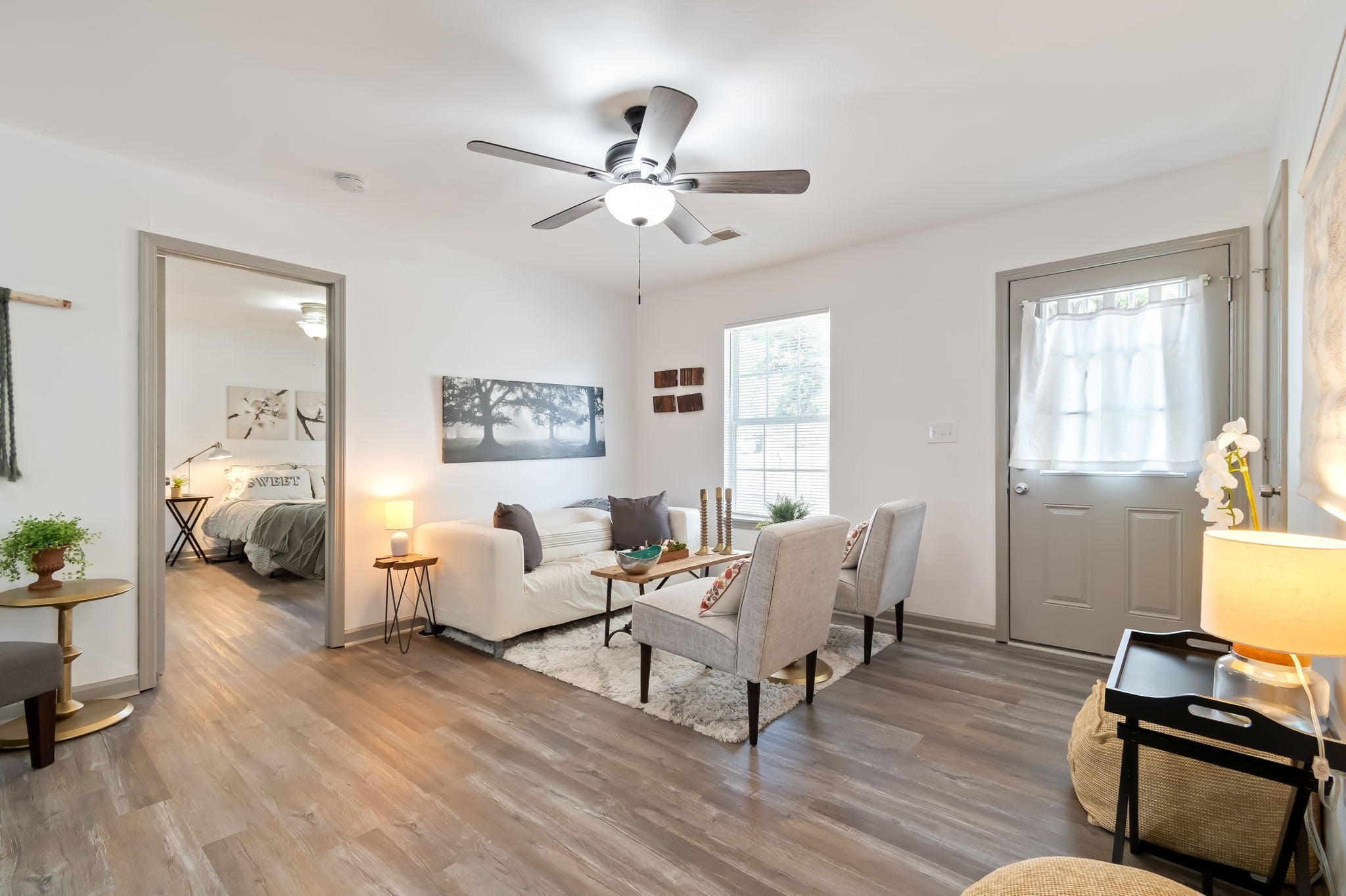 3-bed home for sale in Nashville, TN 37207, 2674 Old Matthews Rd Living room with wood-look vinyl plank floors, gray upholstered chairs, a white sofa and a doorway to a bedroom