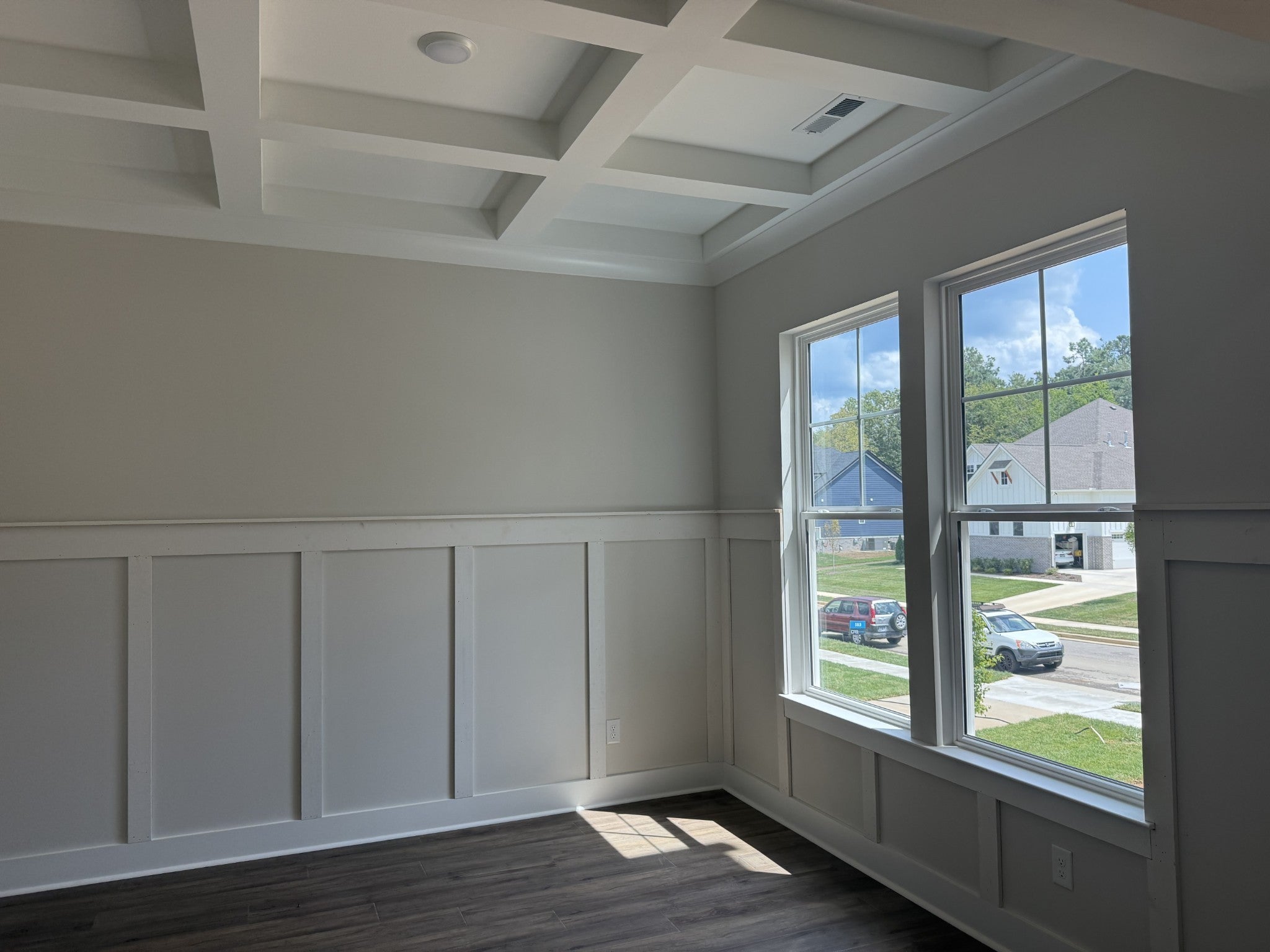 Room with white wainscoting, dark wood floors and two large windows overlooking the street