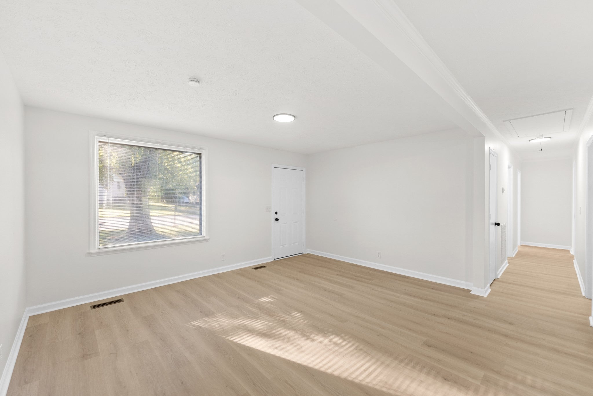 3-bed home for sale in Nashville, TN 37218, 4122 Boyd Dr Empty living room with light wood-look flooring, a large window and a white door, with a hallway visible to the right