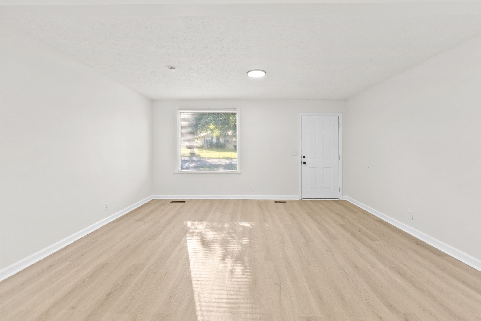 3-bed home for sale in Nashville, TN 37218, 4122 Boyd Dr Empty room with light wood-look flooring, a window with a view of trees and a white exterior door on the right wall