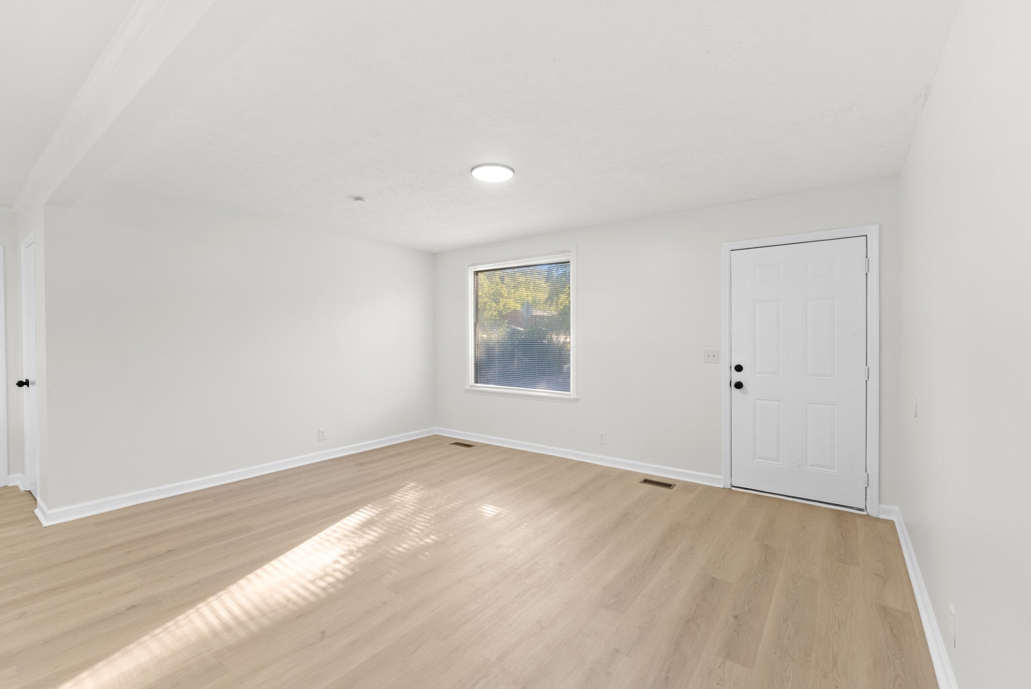 3-bed home for sale in Nashville, TN 37218, 4122 Boyd Dr Empty room with light wood-look flooring, a window with trees outside and a white six-panel door on the right wall