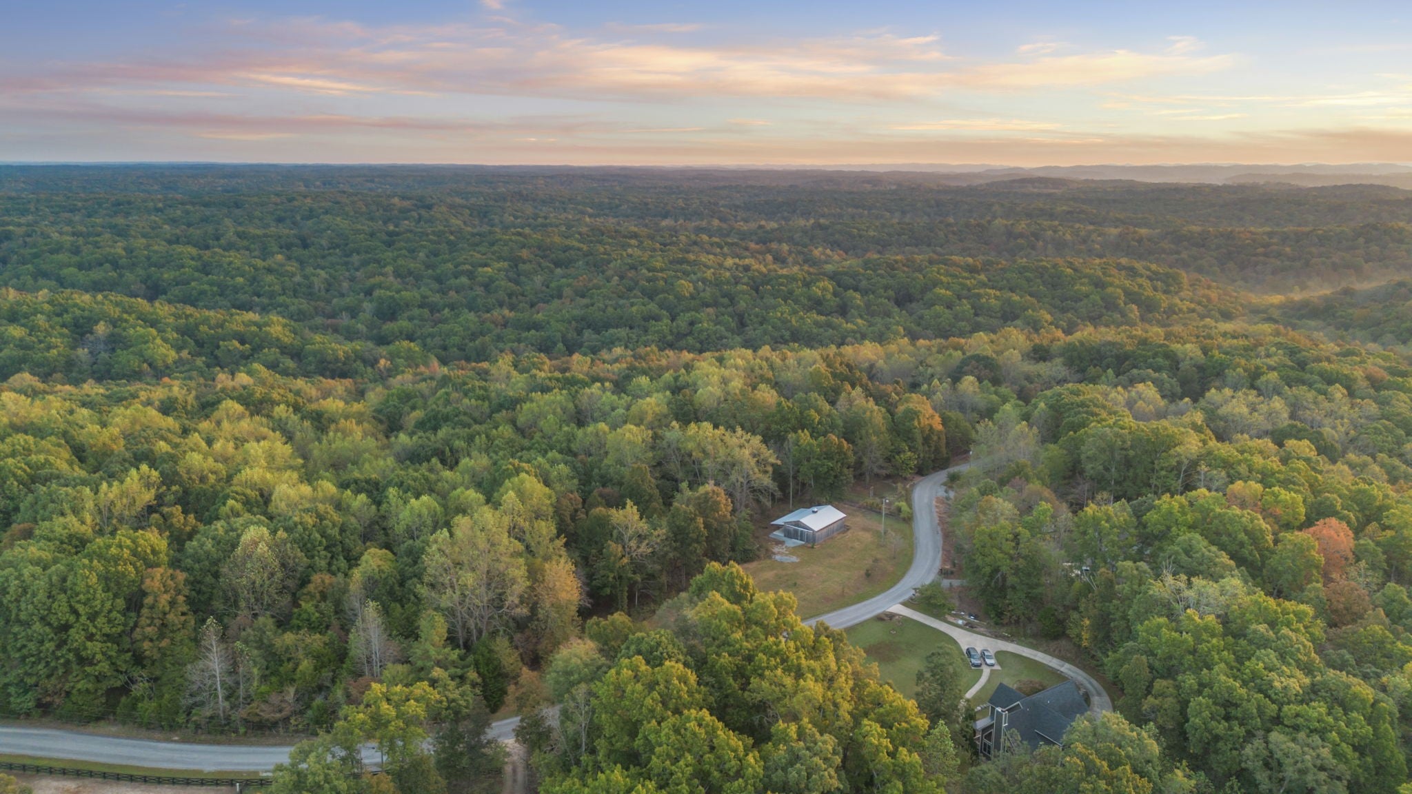 Aerial view of a winding road through wooded hills, with a barn on a cleared parcel beside the road