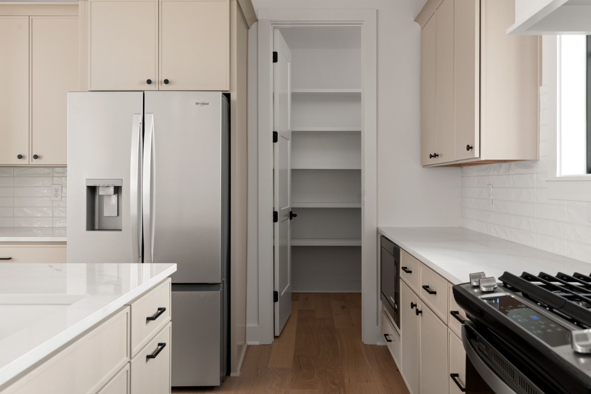 Kitchen with a stainless steel refrigerator, built-in pantry shelving and cream cabinets beside a gas range