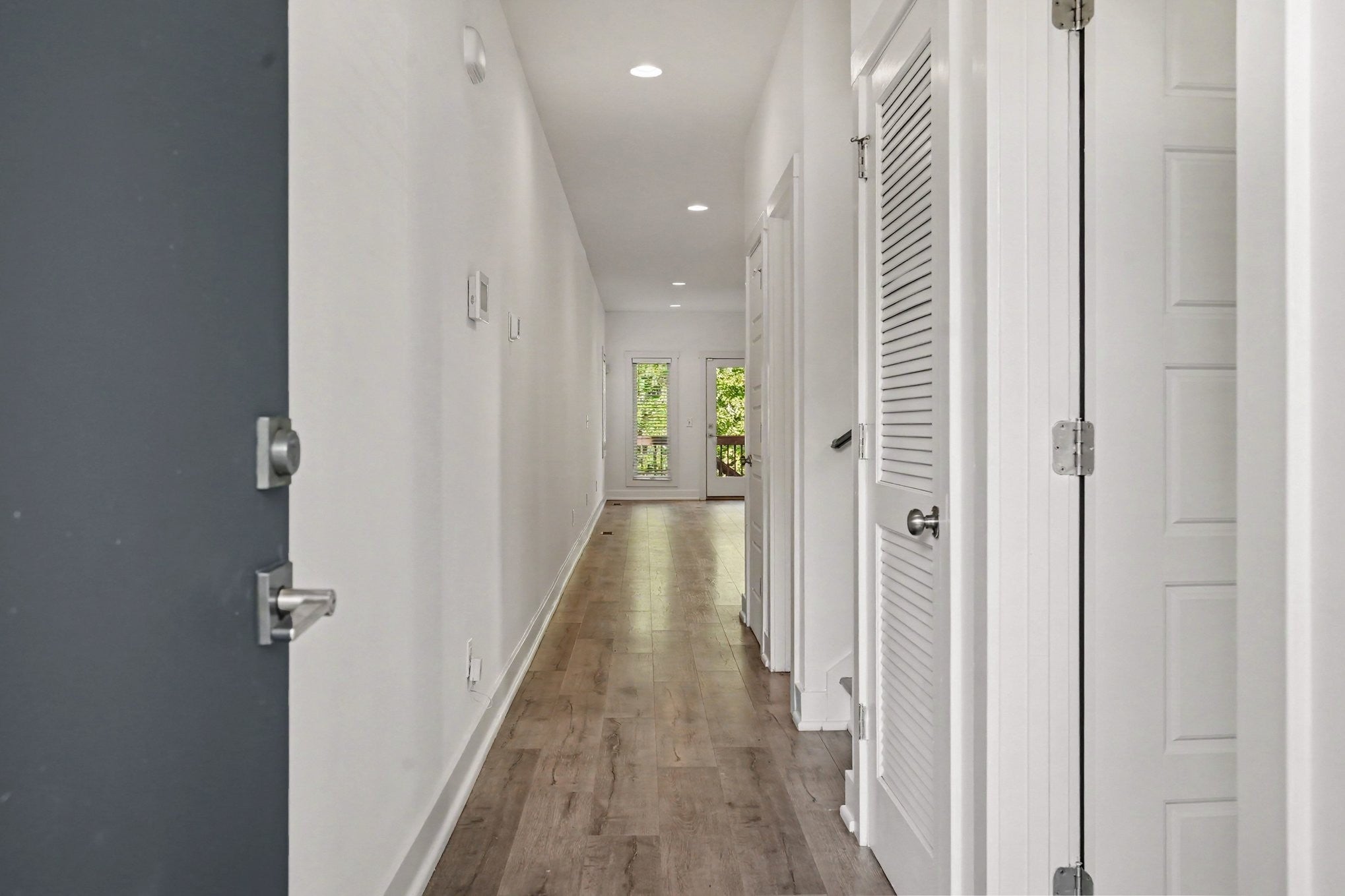Hallway with wood-look vinyl plank floors, white walls, recessed lighting and a glass door at the far end
