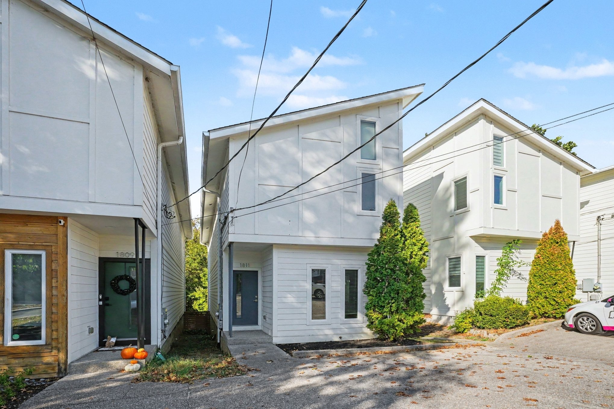 Wide view of the white townhome front with a gravel drive, a covered walkway and neighboring two-story townhomes