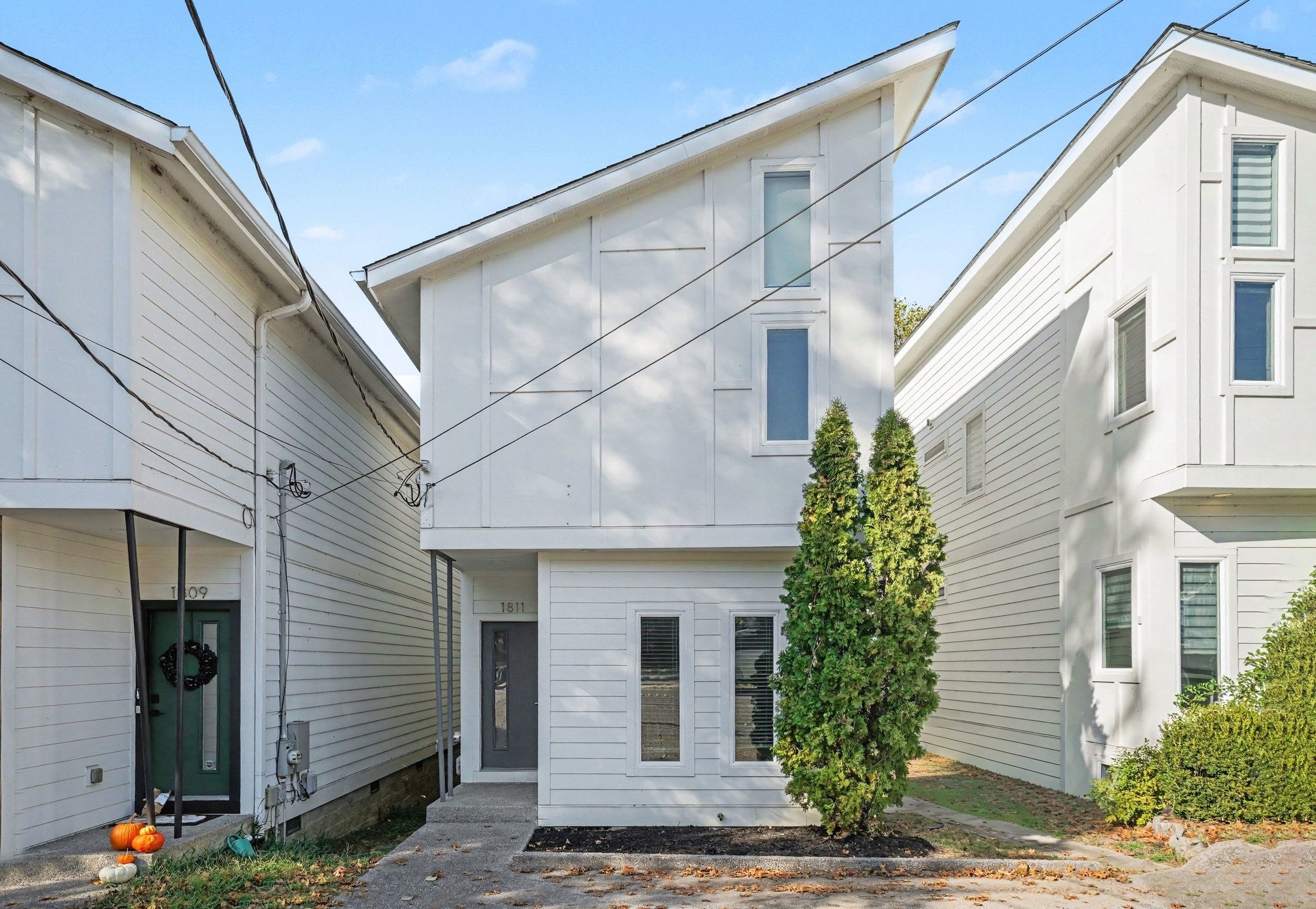Front facade of a white two-story townhome with a gray entry door, tall narrow windows and an evergreen shrub by the walkway