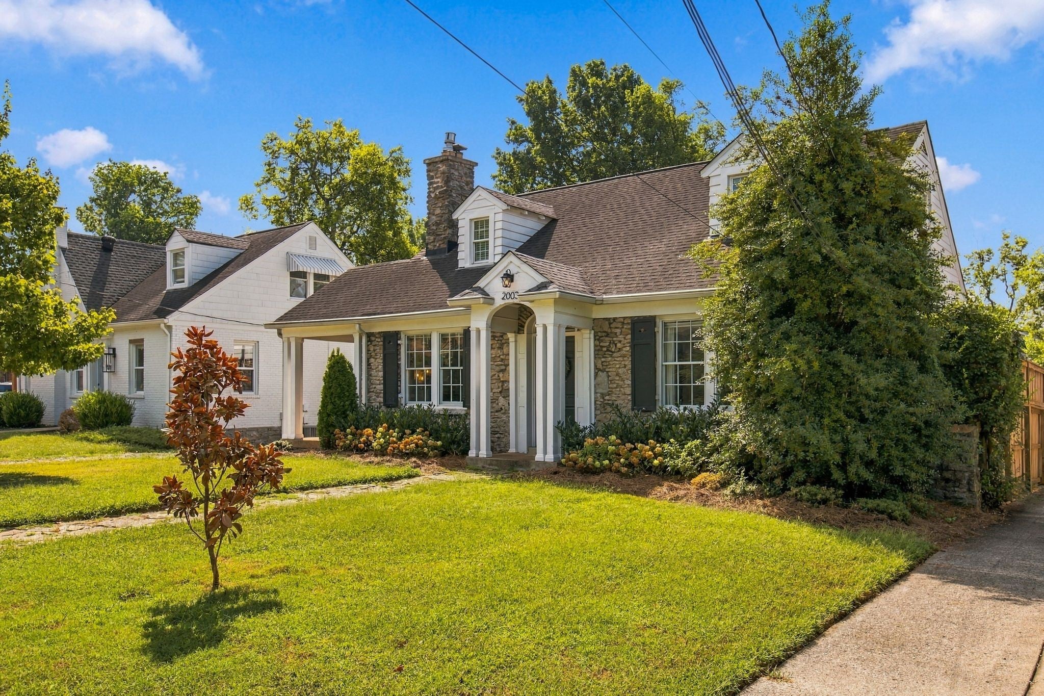 4-bed home for sale in Nashville, TN 37212, 2003 Sweetbriar Ave Side view of a stone and white cottage with a covered side porch, shuttered windows and a lawn along the walk