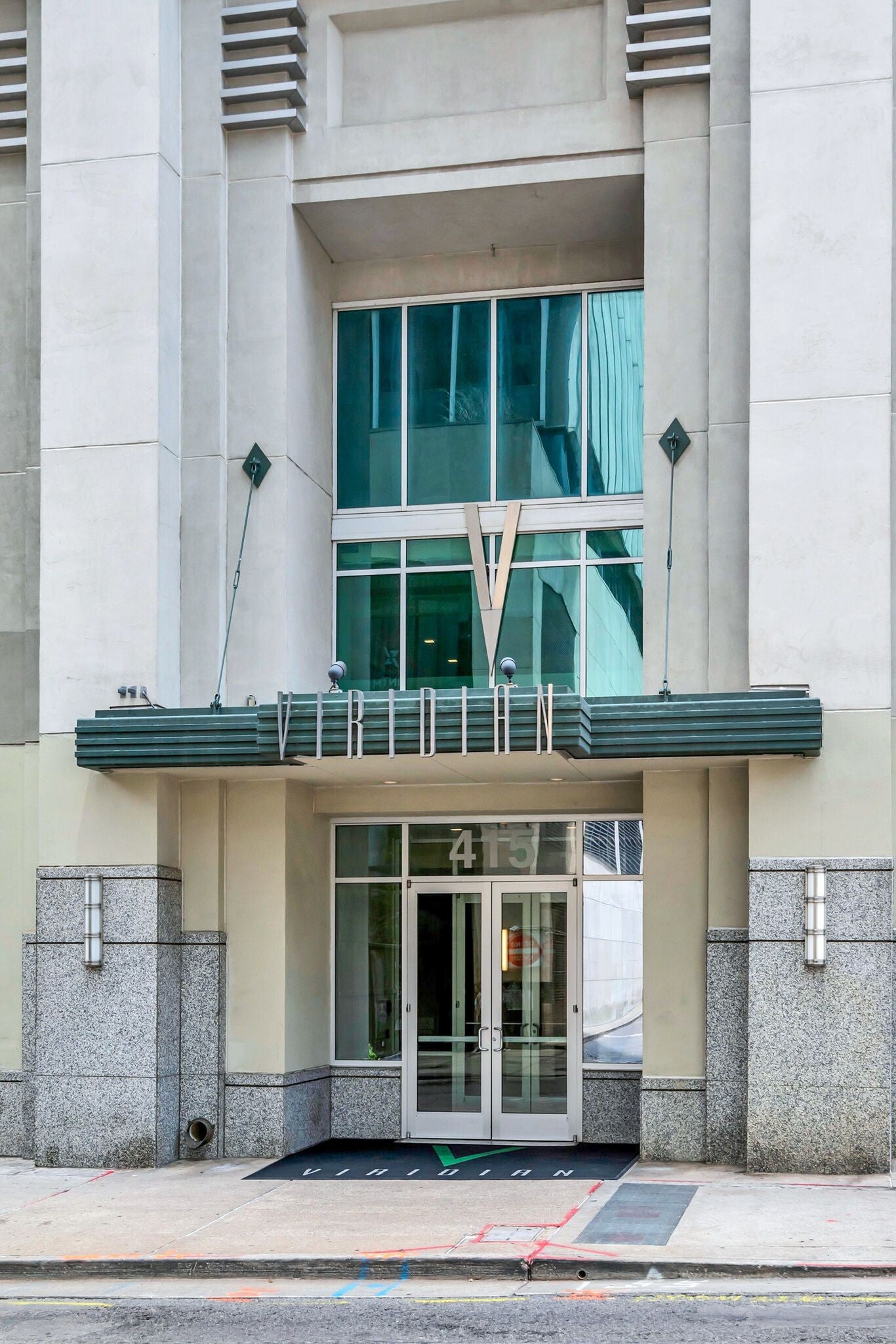 Building entrance with a green canopy, metal lettering, double glass doors and stone pilasters at the base