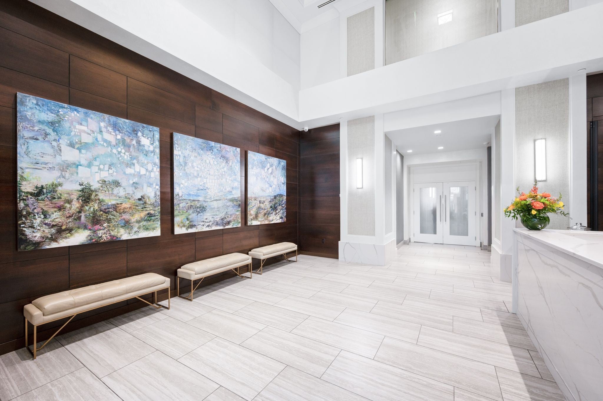 Lobby seating area with three large abstract paintings above cushioned benches and a wood paneled wall