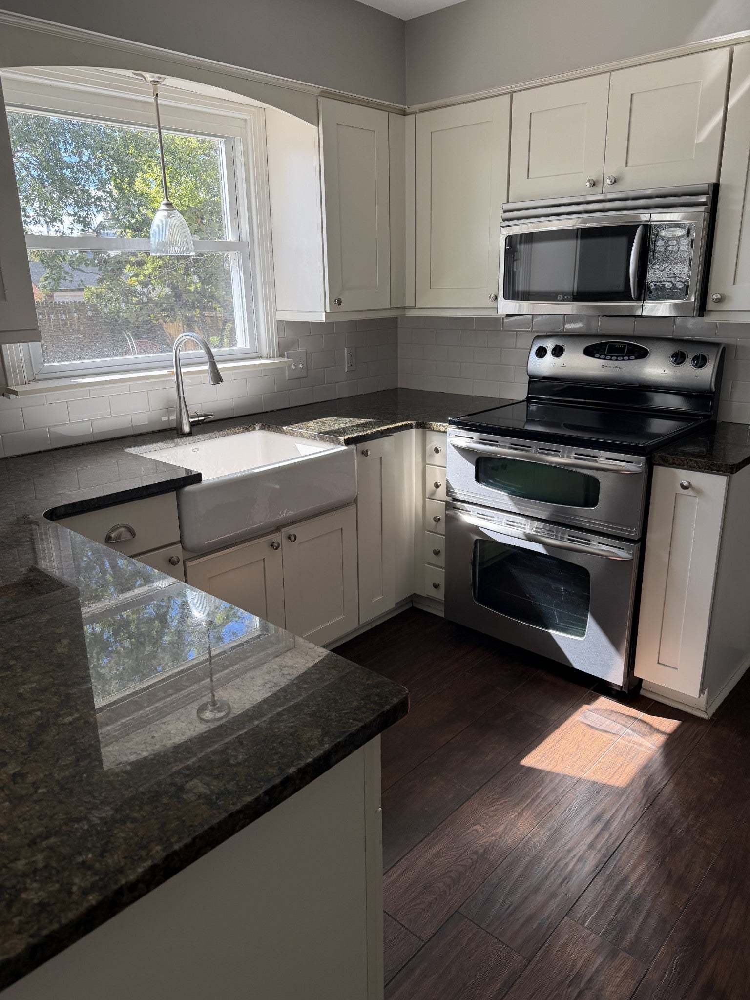Kitchen with dark stone countertops, white shaker cabinets, a farmhouse sink and stainless steel range