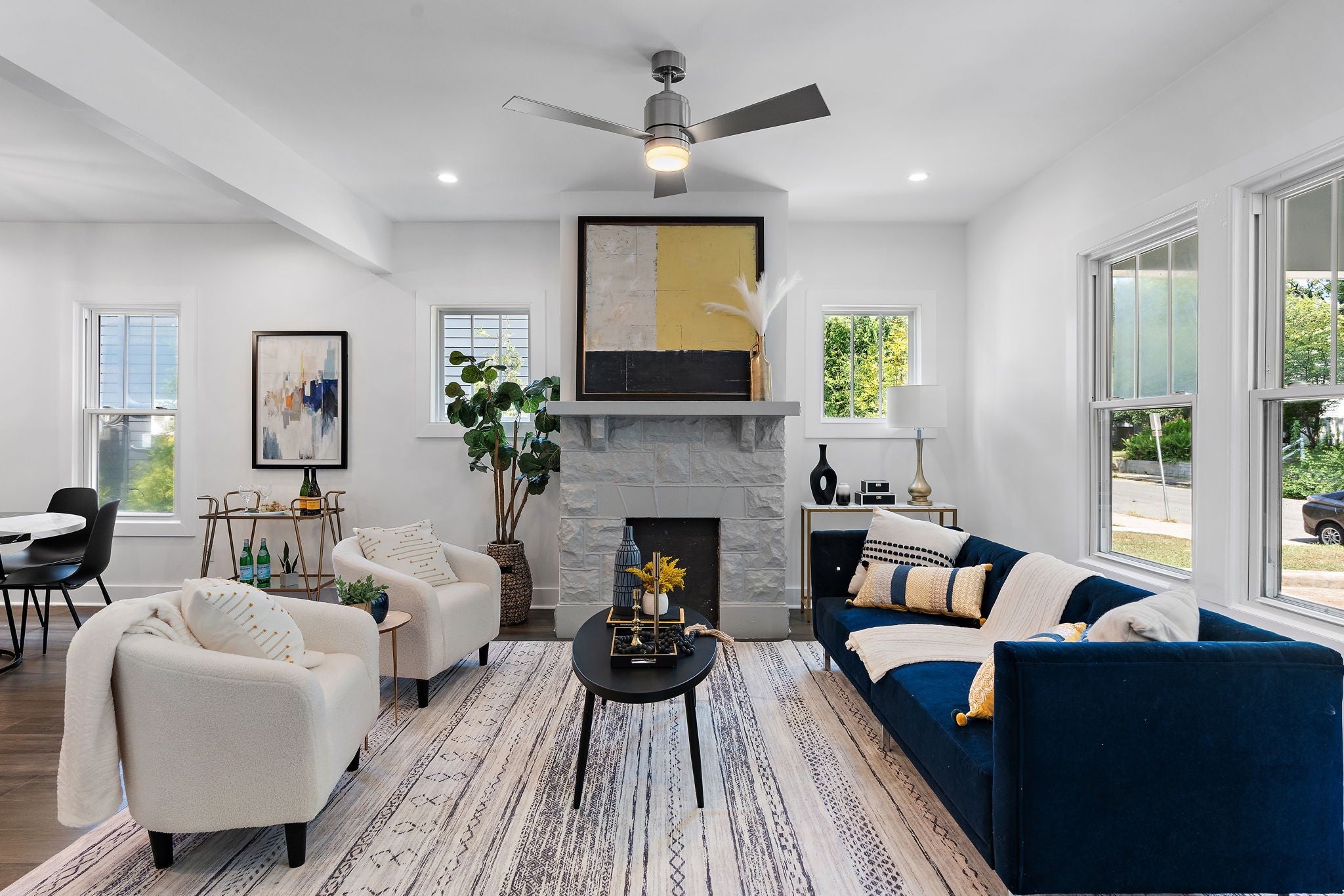 Living room with a stone fireplace, a navy velvet sofa, a ceiling fan and wood floors