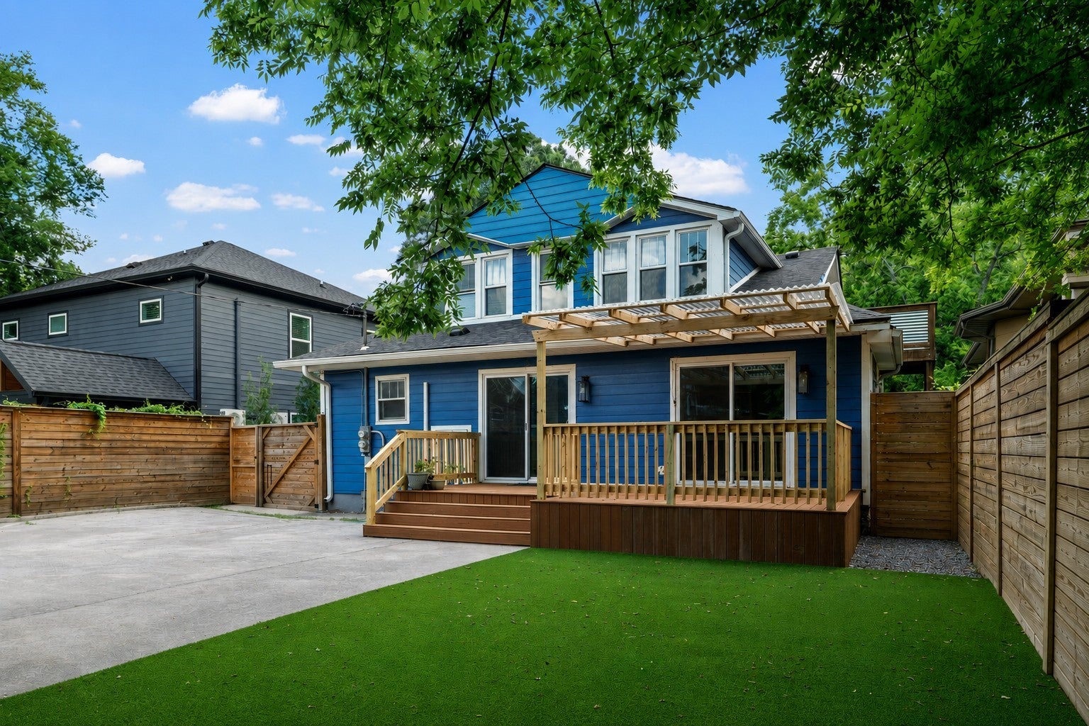 Back of the house with blue lap siding, a wood deck with a pergola and a turf back yard beside a privacy fence