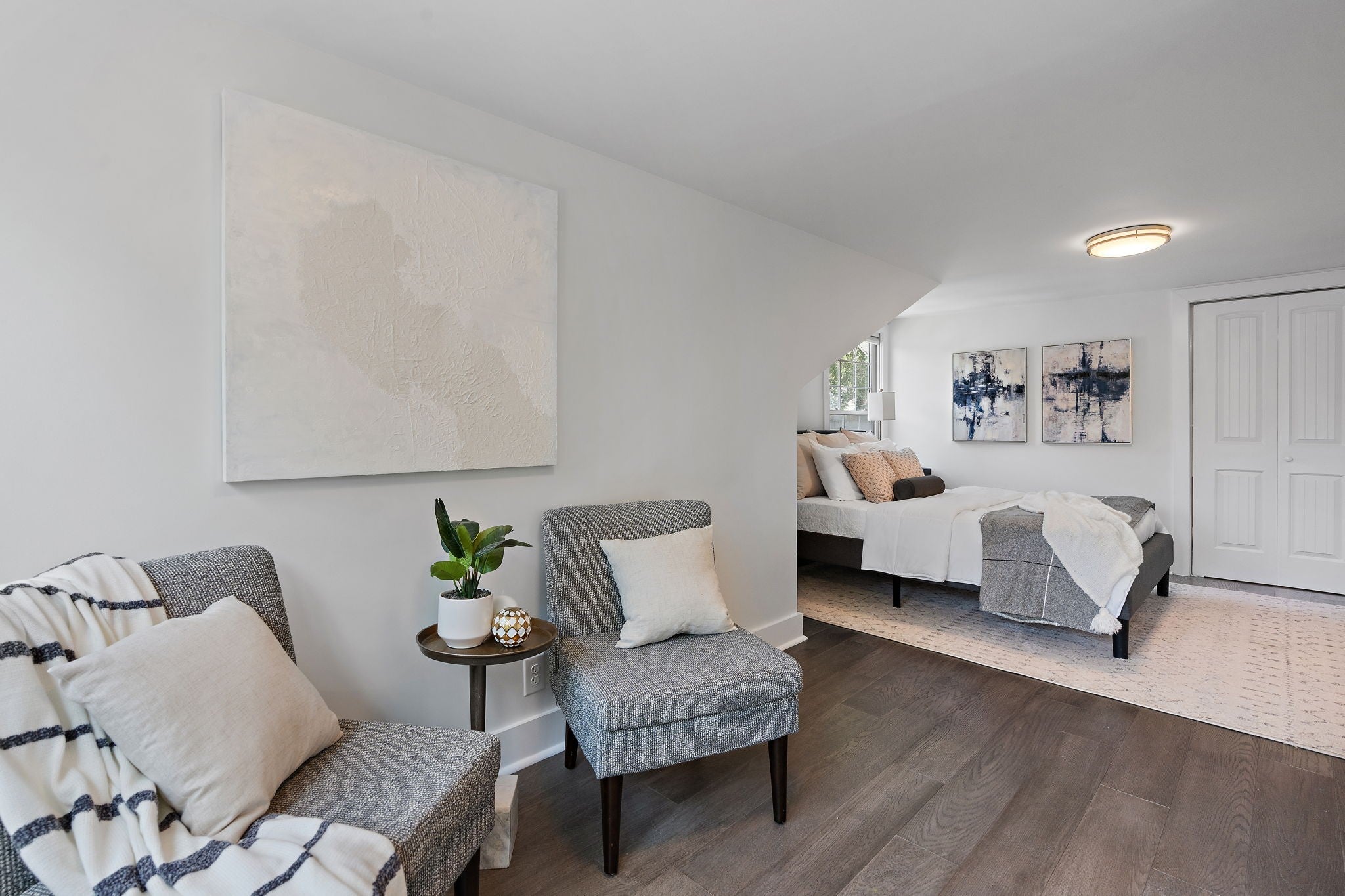 Upstairs bedroom with sloped ceilings, a seating area with two chairs, wood floors and a double-door closet