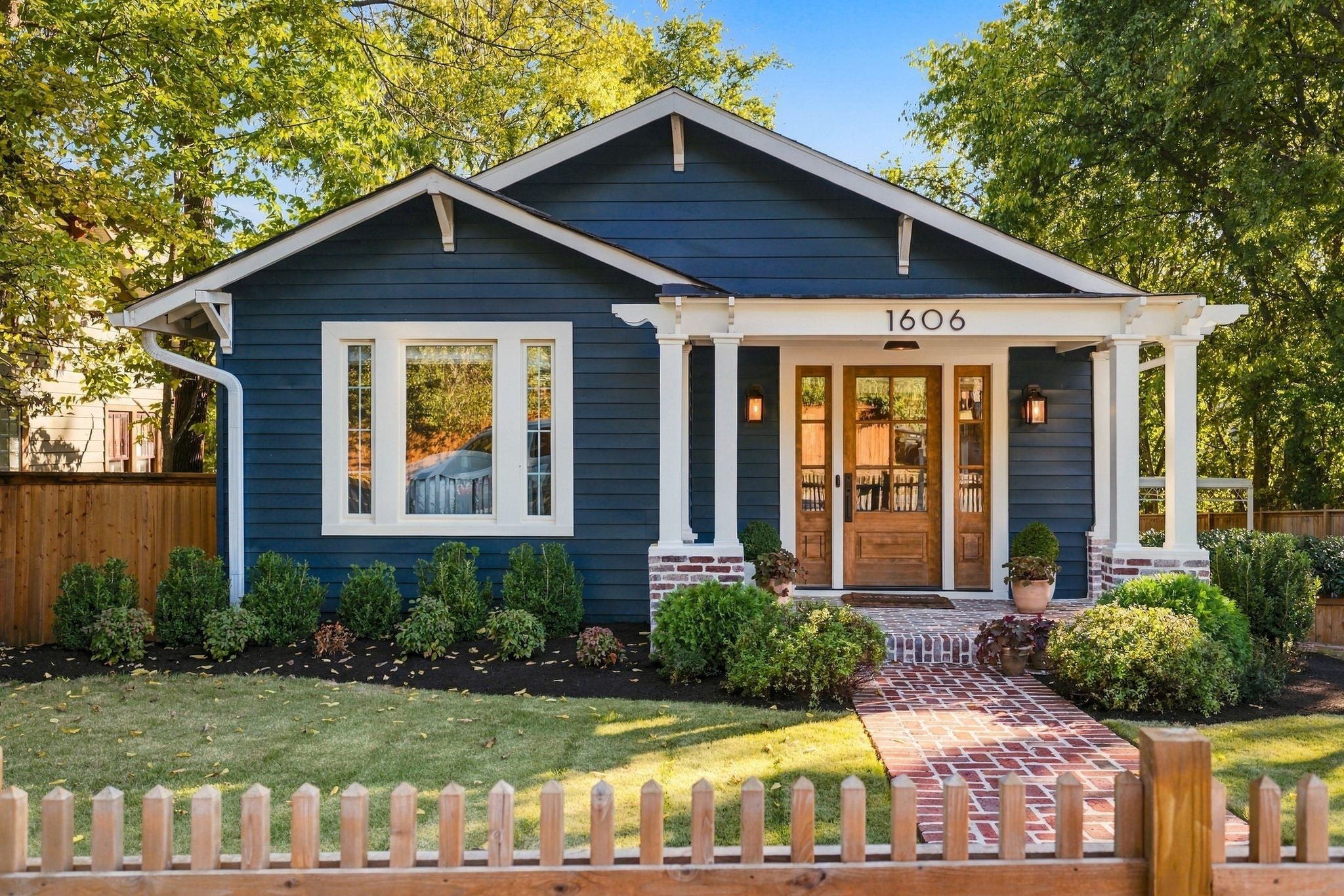 Front entry with white porch columns, a wood door with glass panels and lantern lights beside it, and a brick walkway