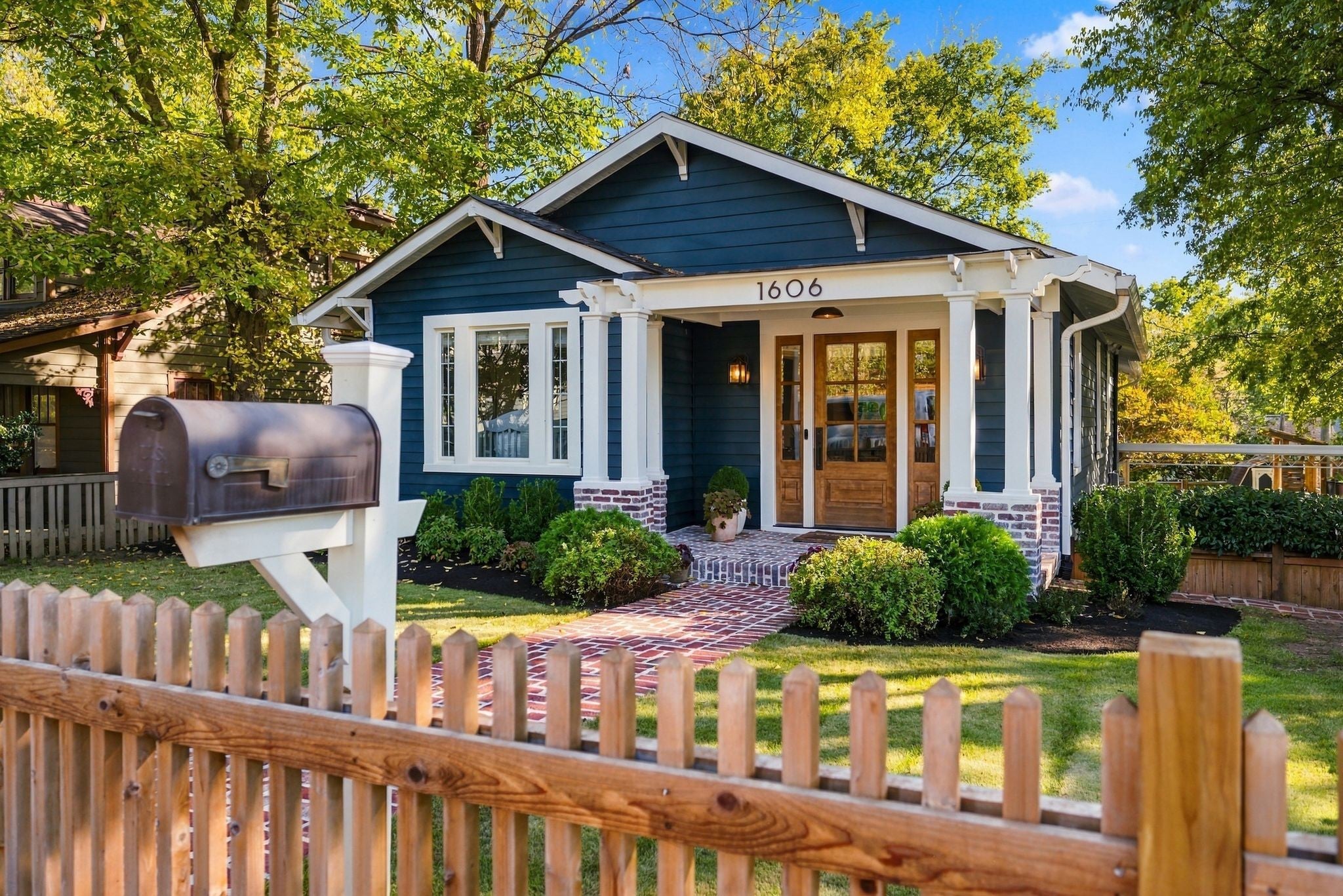 Front yard with a black metal mailbox, white post, picket fence and brick walkway beside the blue house