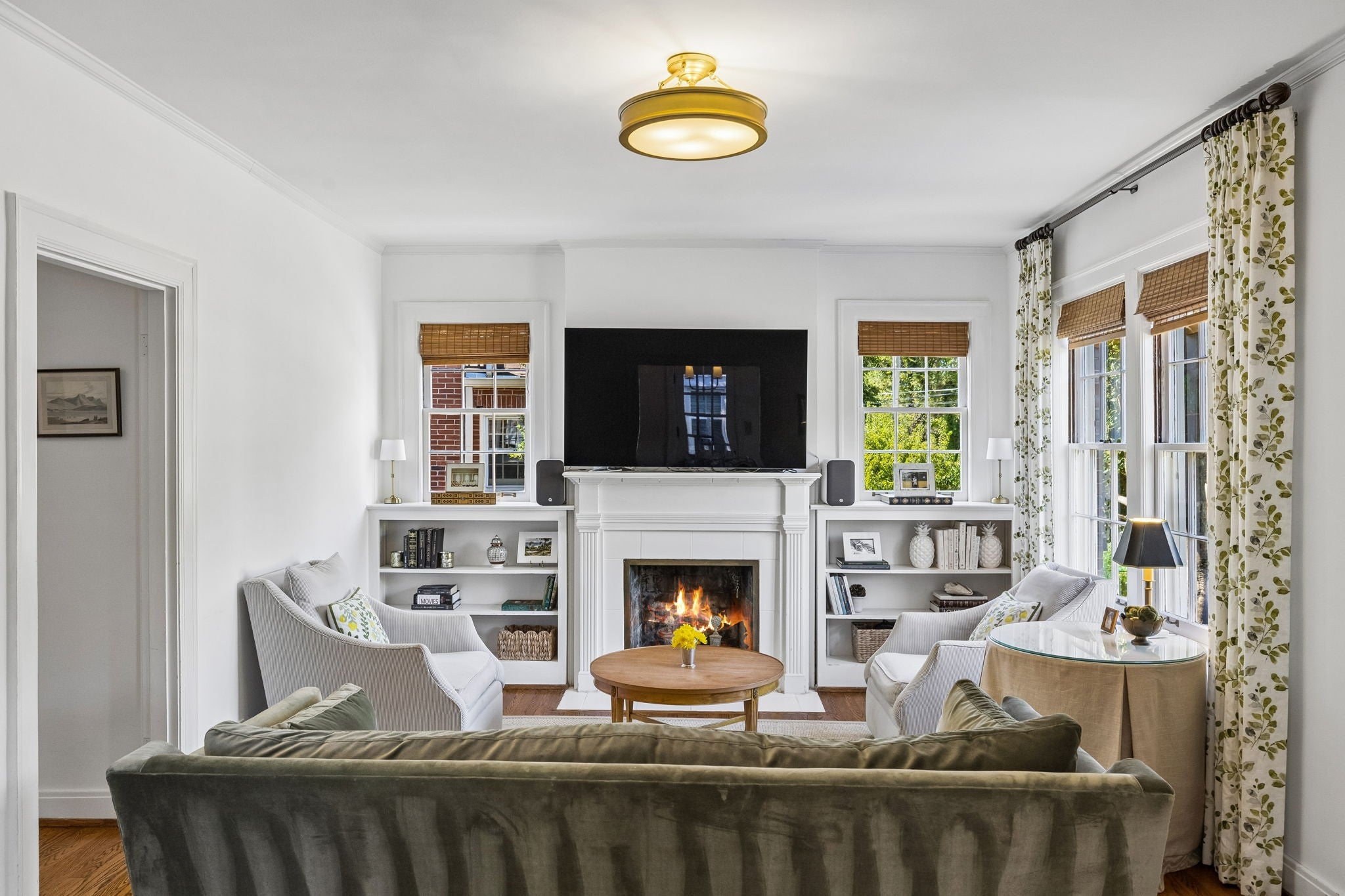 Living room with a white fireplace, built-in bookshelves on each side and windows with patterned drapes