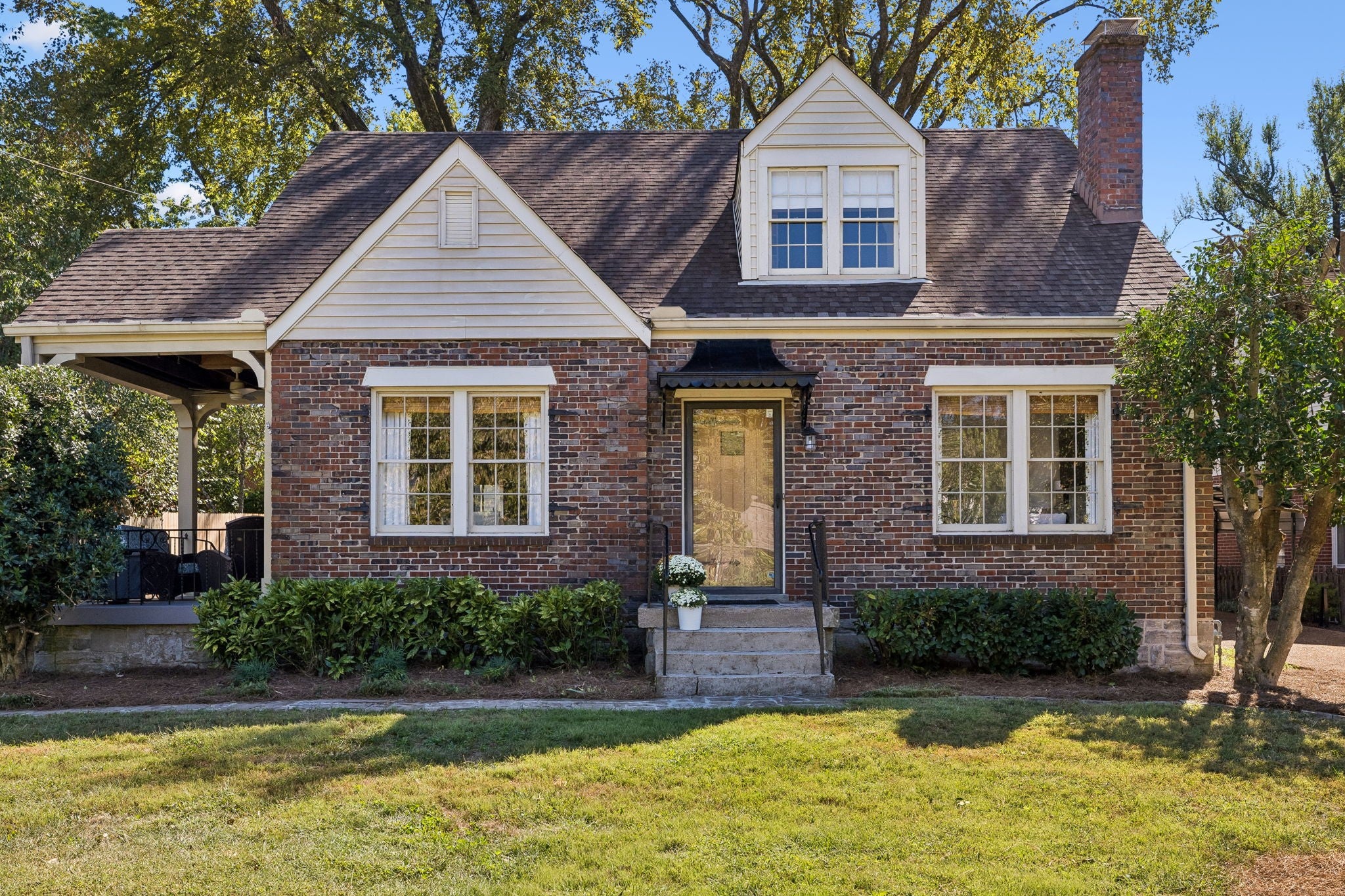 Front facade with light-framed double-hung windows, a wood door with a glass panel and shrubs along the brick base
