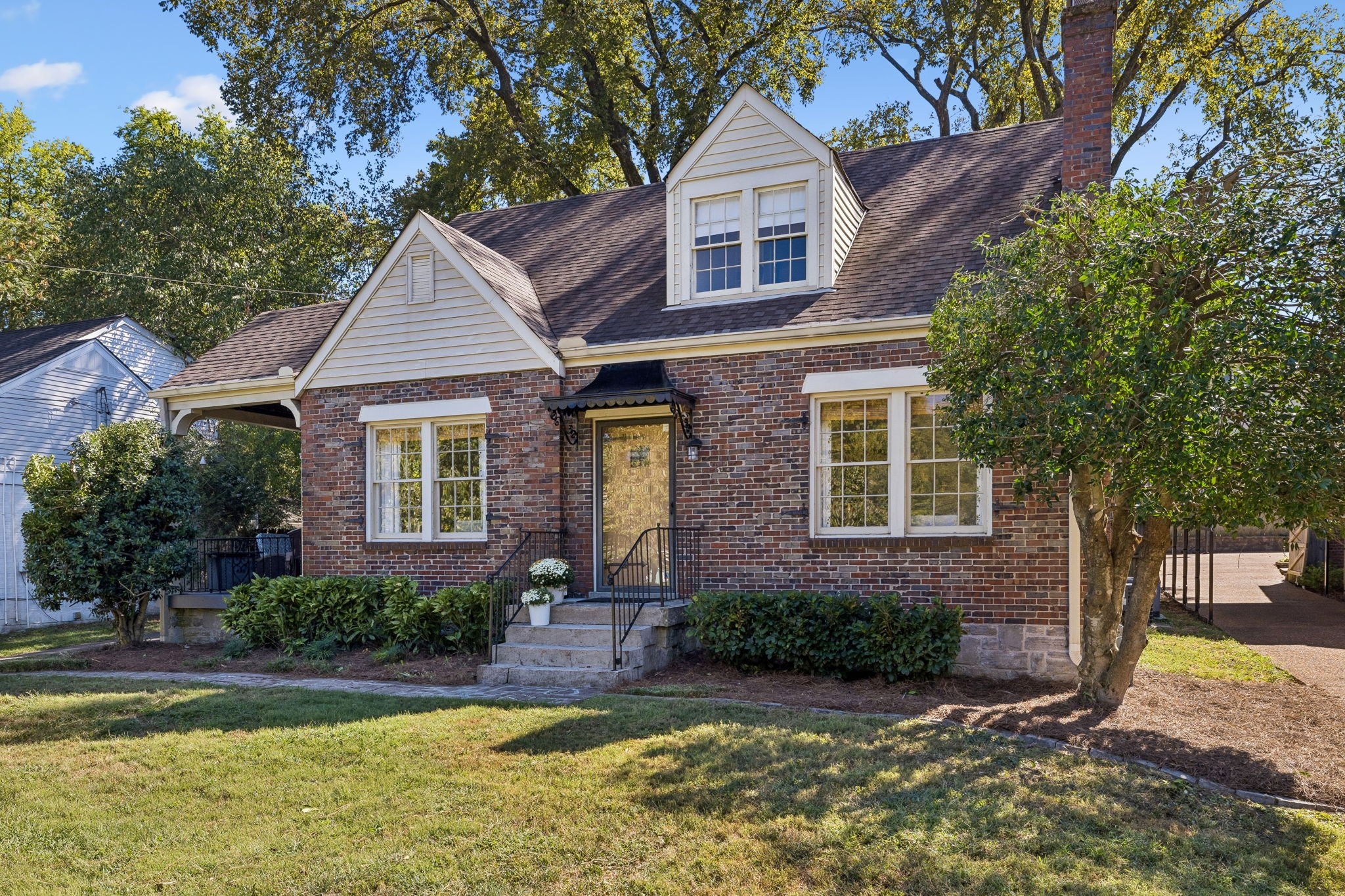 Brick front entry with a dormer above, black railings on the front steps and a dark awning over the door