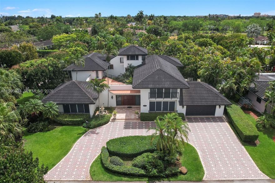 A home defined by space, light, and architectural character—designed for both comfortable living and effortless entertaining, tucked within the desirable enclave of Windemere Woode just off Sunset Drive. Considered one of the premier homes in the community, this home offers a thoughtful layout and inviting scale throughout. At the center, a striking interior atrium with a tranquil waterfall brings natural light and a sense of calm, with the main living areas oriented to capture its views. The home offers two levels plus a third-floor private retreat or study with a balcony. The main level features a formal living room w/ wood beam ceilings, formal dining, and a spacious family room with custom built-ins. The kitchen serves as a central gathering space, offering a generous eat-in breakfast area and bar, with views to outdoor areas, including a covered summer kitchen, oversized swimming pool - patio, and mature mango trees. A first-floor bedroom and plus a den, and flexible living spaces support a variety of lifestyles. Upstairs, find the primary suite and 3 additional bedrooms with connecting bathrooms. Expansive north and south-facing balconies provide additional outdoor living.  Important updates have been completed, including a newer roof and A/C systems, and impact windows and doors. Drainpipes are PVC, and whole house generator. Elevator plans available. This presents a rare opportunity to cosmetically tailor a home of this scale and character to your own vision.