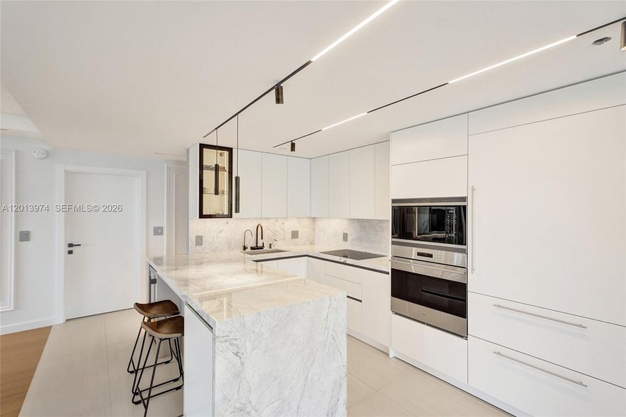Completely renovated one year ago by a professional European designer, this stunning 3-bedroom, 3.5-bath residence in an exclusive boutique building of only 15 units is one of the most refined offerings in Bay Harbor Islands. Every detail was custom-designed with no expense spared — featuring bespoke European millwork, integrated custom built-in furniture with LED accents in every room, European cabinetry with Blum hardware, a dramatic quartzite waterfall island, marble slab backsplash, full Wolf appliance suite, large-format porcelain slab TV panel and accent walls throughout, white oak floors, state-of-the-art track lighting, Somfy motorized smart blinds, and a fully integrated smart home system with automated lighting. The open living and dining area is anchored by a custom fluted accent wall with backlit porcelain slab feature. The spa-caliber primary suite offers a full bathroom with dual vessel sinks and frameless glass shower. All three bedrooms feature en-suite baths for ultimate privacy, every one finished in large-format Porcelanosa tile and equipped with electronic heated bidet toilets. Every bedroom includes a custom walk-in closet with Blum hardware and LED lighting on every shelf.
Wraparound balconies accessible from every room deliver 567 sq. ft. of total outdoor living space — perfect for entertaining or relaxing in the open air. Building amenities include a rooftop pool, private gym, and two assigned parking spaces.
