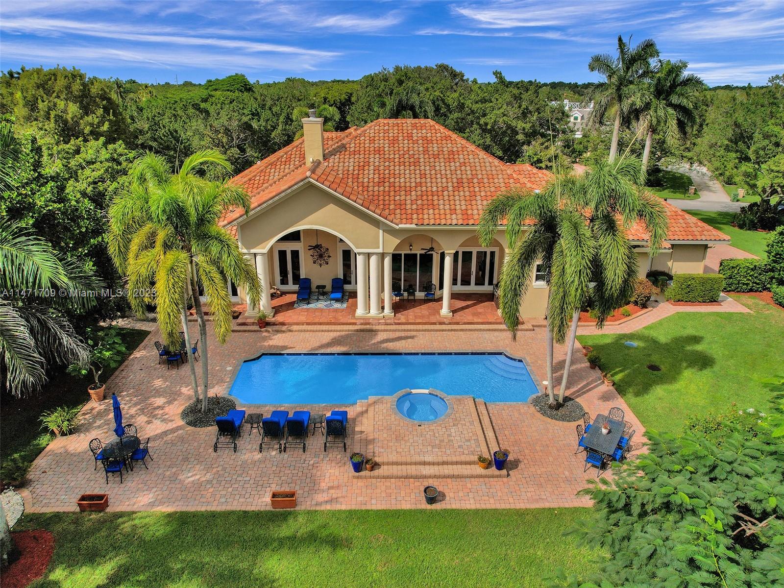 Situated in the esteemed Windmill Lake Estates, this 4-bed, 4.5-bath sanctuary exudes luxury and privacy. A grand circular driveway and 3 car garage greet you, while serene water views and lavish lap pool within lush landscape define the outdoor experience. Marble floors, fireplace, and French doors elevate the main living areas. High ceilings accented by crown molding and gourmet kitchen—outfitted with a wood island, custom cabinets, and high-end appliances. The owner's suite is a private retreat with hardwood floors, plantation shutters, and patio access with a marble-clad primary bath with dual sinks, a Jacuzzi tub, and a shower. Well-appointed office with its own half bath. New impact-resistant windows and doors and a new roof are the finishing touches on this luxurious abode.