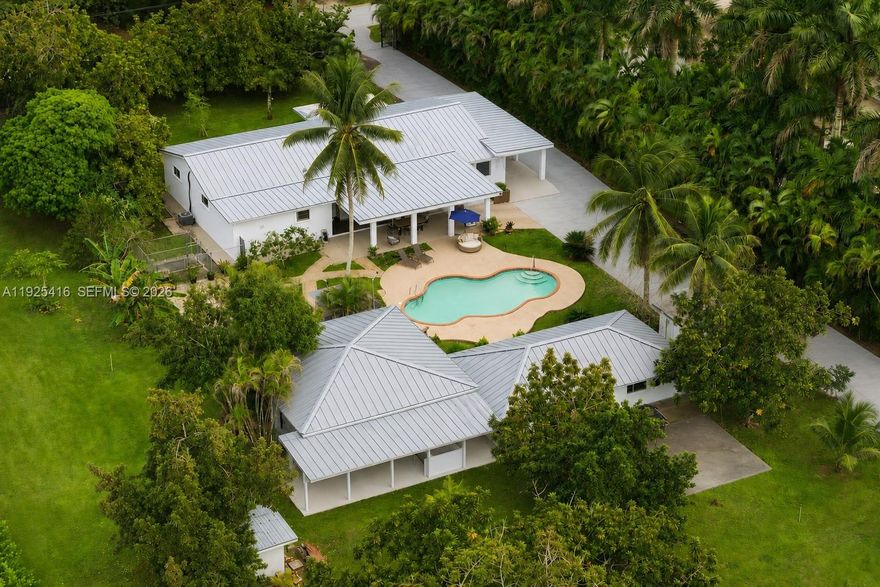 Tucked behind lush landscaping in the heart of the Redlands, this 2.42-acre tropical retreat offers a rare blend of serenity, recreation, and resort-style living. The 3-bed, 2-bath main residence features spacious interiors with open living areas, garden views, and a seamless indoor-outdoor flow. Across from the main house sits a detached game room/studio suite with full bath, plus a separate entertainment pavilion which boasts a bar and grill, as a covered lounge. Outside, enjoy a sparkling kidney-shaped pool surrounded by fruit trees, flowering gardens, and shaded patios. Located at the back of the property, sits a 2-car garage with a connected 1-bed/1-bath apartment. The grounds are a horticultural haven with more than a dozen varieties of tropical fruit trees, mature palms, and lush plantings that create a true sense of escape. Designed for both relaxation and activity, the property includes stables to board 5-horses, and a rare private indoor sports shooting range. Additional features in the main house include a formal dining area, dual primary suites, whirlpool tub, accordion shutters, and a full-house generator for peace of mind. As a family compound, private getaway, or equestrian paradise, this exceptional estate delivers a unique lifestyle immersed in the natural beauty and privacy of South Florida’s iconic Redland agricultural community.