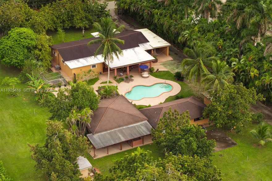 Tucked behind lush landscaping in the heart of the Redlands, this 2.42-acre tropical retreat offers a rare blend of serenity, recreation, and resort-style living. The 3-bed, 2-bath main residence features spacious interiors with open living areas, garden views, and a seamless indoor-outdoor flow. Across from the main house sits a detached game room/studio suite with full bath, plus a separate entertainment pavilion which boasts a bar and grill, as a covered lounge. Outside, enjoy a sparkling kidney-shaped pool surrounded by fruit trees, flowering gardens, and shaded patios. Located at the back of the property, sits a 2-car garage with a connected 1-bed/1-bath apartment. The grounds are a horticultural haven with more than a dozen varieties of tropical fruit trees, mature palms, and lush plantings that create a true sense of escape. Designed for both relaxation and activity, the property includes stables to board 5-horses, and a rare private indoor sports shooting range. Additional features in the main house include a formal dining area, dual primary suites, whirlpool tub, accordion shutters, and a full-house generator for peace of mind. As a family compound, private getaway, or equestrian paradise, this exceptional estate delivers a unique lifestyle immersed in the natural beauty and privacy of South Florida’s iconic Redland agricultural community.