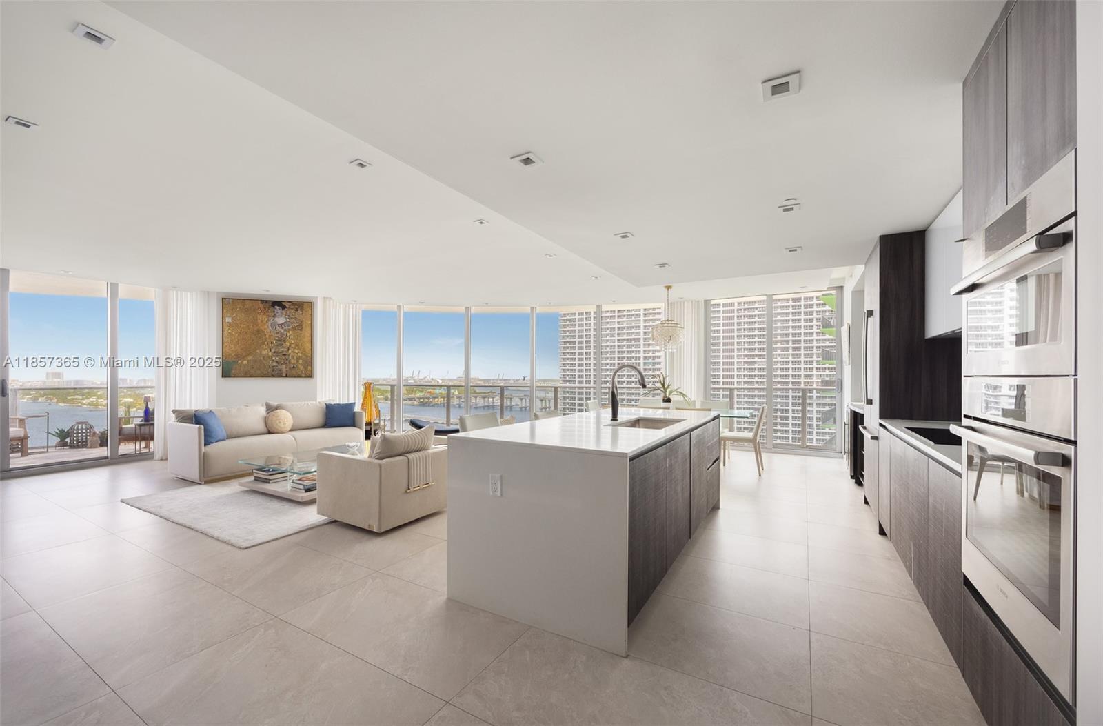 This upscale corner residence at Aria On The Bay combines luxury, comfort, and breathtaking views of the bay and Miami skyline. Featuring 3 bedrooms, a den, and 4 bathrooms, the unit offers both style and functionality. Two private elevators open to a private foyer, ensuring exclusive access and convenience.
The spacious living area is enhanced by floor-to-ceiling windows, a custom drop ceiling, smart home, porcelain flooring, integrated speakers in every room and a bespoke bar area, all beautifully furnished with custom pieces by MORADA. Step out onto the expansive wrap-around terrace to enjoy panoramic city and water views. The unit features numerous high-end features. *Furniture available for separate purchase.