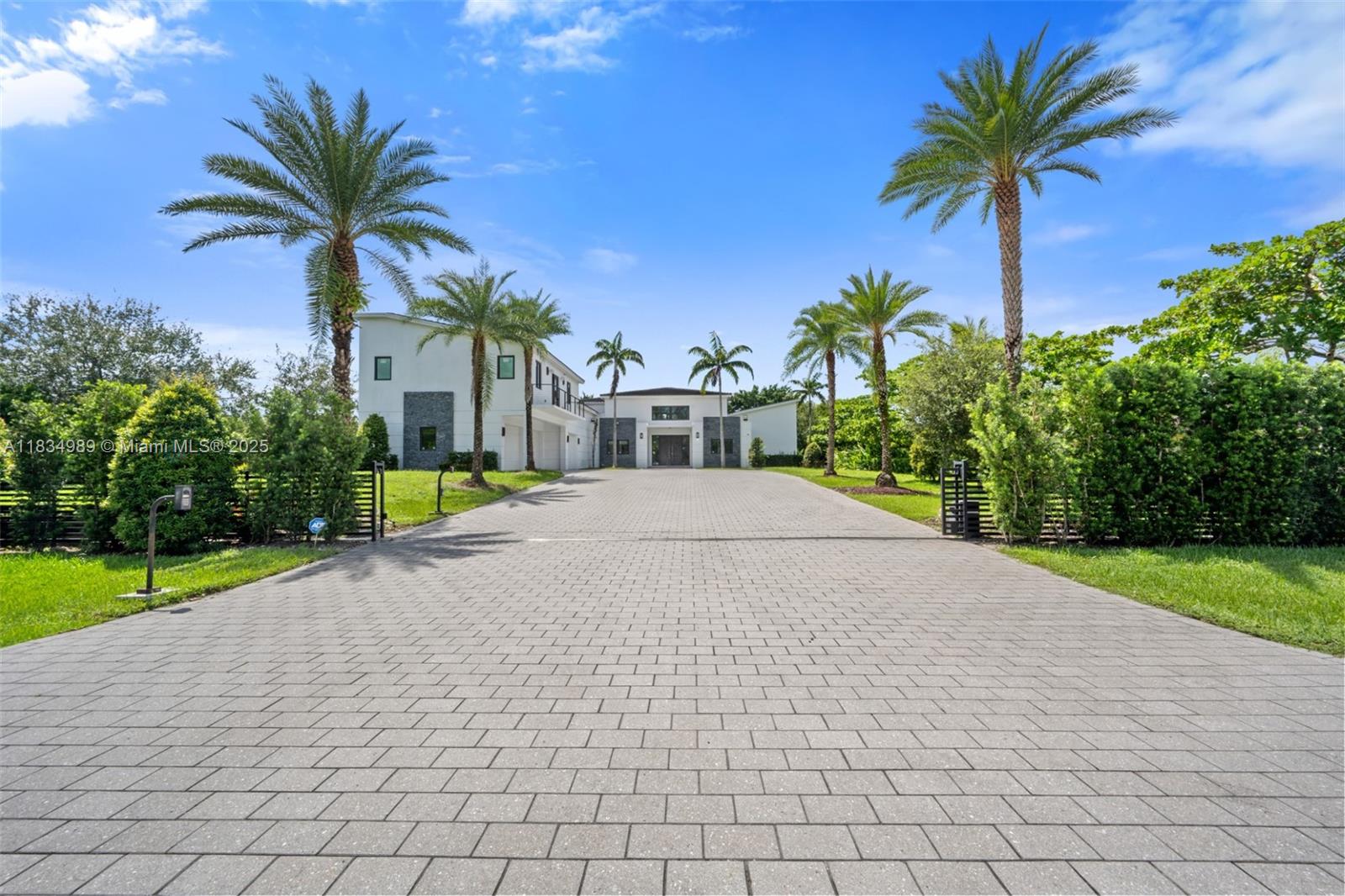 Modern masterpiece on expansive grounds, boasting soaring 20-ft ceilings, sleek porcelain floors, and a chef’s kitchen with custom cabinetry and quartz counters. Six spacious bedrooms each offer private ensuite baths and custom walk-in closets. The lavish primary suite features a serene sitting area, dual walk-in closets (his and hers), and a luxe glam room with built-ins for shoes, handbags, and makeup. A private elevator provides access to the second level, where you’ll find a stunning home theater, bar, and kitchen. Outdoors, indulge in resort-style living with a saltwater pool, spa, summer kitchen, covered terrace, and an impressive driveway with a 3-car garage. Smart, energy-efficient, and built for ultimate contemporary living.