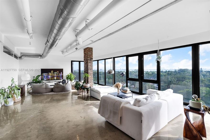 Discover this one-of-a-kind loft-style 4BD/3.5BA residence—currently configured as a 3-bedroom plus storage—offering dramatic open-concept living, sweeping floor-to-ceiling glass, and panoramic views of Biscayne Bay, the Miami skyline, and lush tree canopies. Designed with an industrial-modern aesthetic, the home showcases exposed ducts, polished concrete floors, brick accents, and custom wood millwork throughout. The expansive great room seamlessly integrates living, dining, and an open chef’s kitchen, creating an ideal setting for entertaining. The primary suite delivers a true retreat with incredible natural light, oversized balcony access, and a sculptural soaking tub set against skyline vistas. Multiple lounging areas, flexible spaces perfect for office or creative use, and generous storage enhance daily living. The boutique building features a rooftop dry sauna, pool and is just a 3-minute walk from beautiful Morningside Park—offering an exceptional blend of volume, character, lifestyle, and location at the edge of Morningside and the MiMo District.
