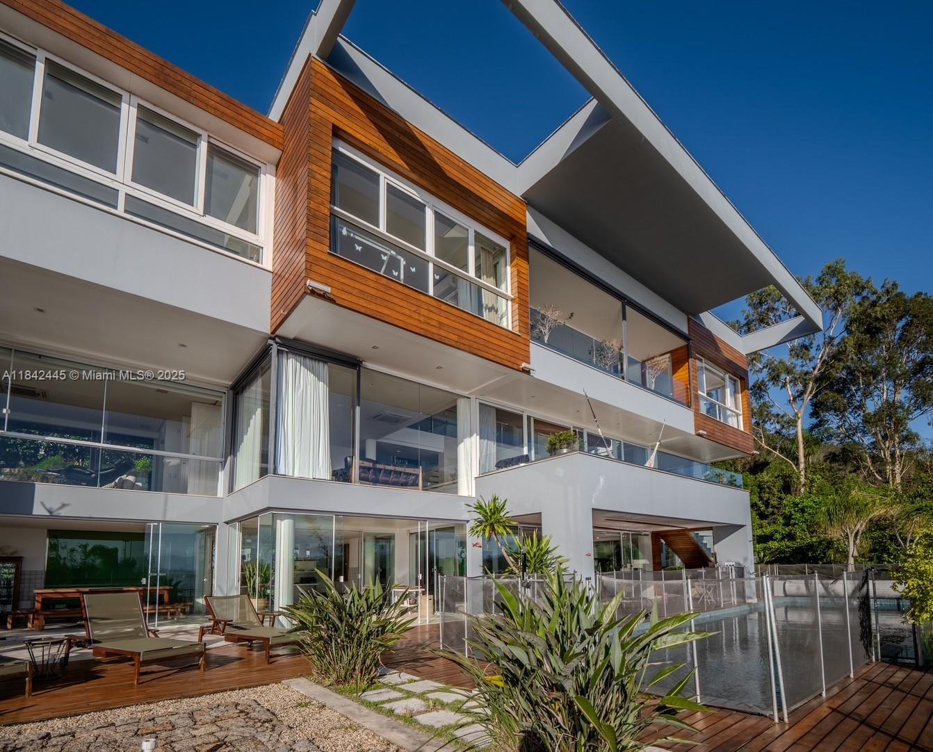 Wonderful luxury mansion in Brazil with three levels and permanent sea view, in a gated community in Cacupé, Florianópolis. Modern architectural design with spacious rooms, 6 suites, club area with barbecue, heated infinity pool, spa, sauna, panoramic elevator, two gyms and exclusive finishing items. Condominium with nautical club with fixed pier with floating deck, helipad, camera monitoring and 24-hour armed concierge, tennis court, forest, trails, gazebo and orchid garden