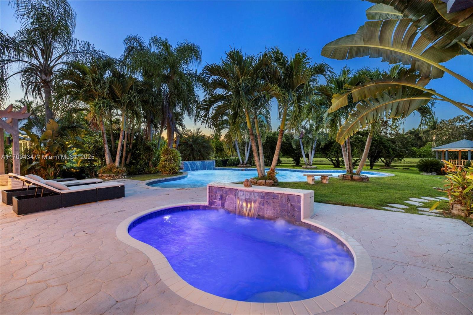 Welcome to this exquisite 3,500+ sq. ft. estate in the prestigious Kapok Village Estates of Davie, FL. Nestled on a lush, private acre with tranquil canal views, this elegant residence offers refined indoor-outdoor living. Highlights include a grand, vaulted-ceiling layout, four bedrooms plus a den, a resort-style oversized pool and spa, a summer kitchen, an expansive yard, and a three-car garage.