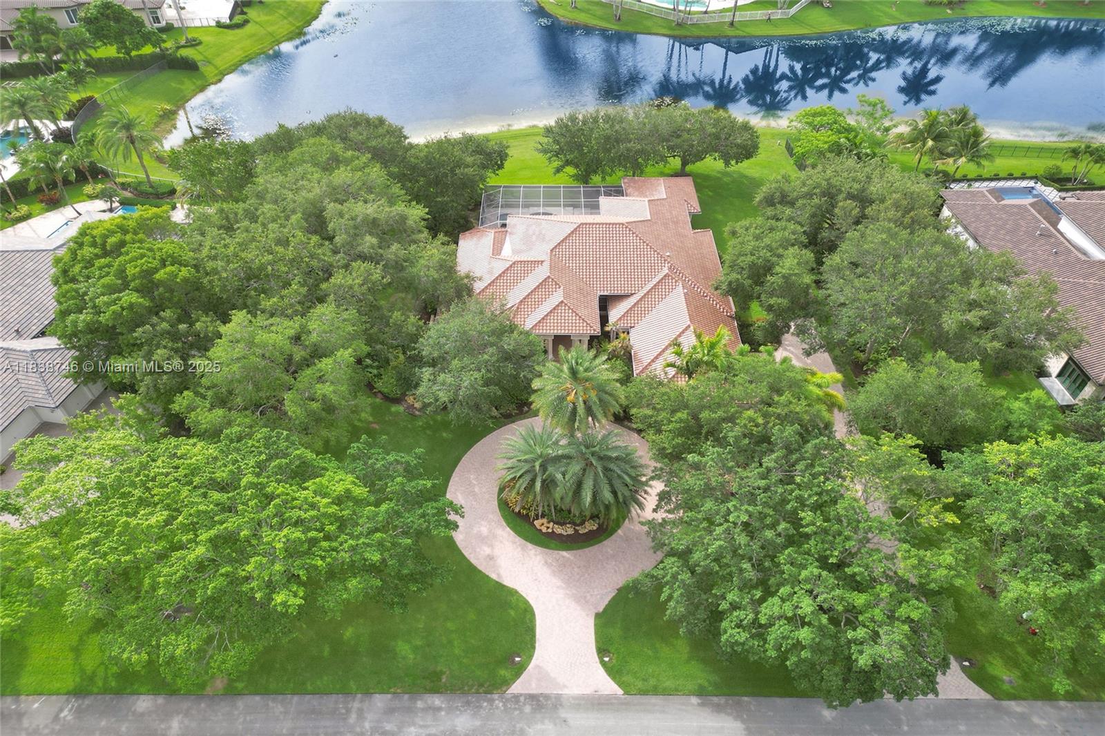 Welcome to Windmill Lake Estates this one-story lakefront estate sits on an expansive 49,796 sq ft lot with 180 feet of panoramic water views. Featuring 5 bedrooms and office, 4 bathrooms, and 4,006 sq ft of living space, this home offers volume ceilings, a brand-new 2024 roof, and neutral tones throughout. Spacious primary suite includes sitting area overlooking the pool and lake views 3 walk-in closets and spa-like bath with whirlpool. Traditional kitchen with wood cabinetry, granite countertops, wall oven, and SS appliances. Enjoy a 3-car side garage, circular driveway, and screened-in pool and spa with serene lake vistas. The lush grounds offer room to expand or create your dream outdoor space. Located in one of Weston’s most exclusive gated communities.